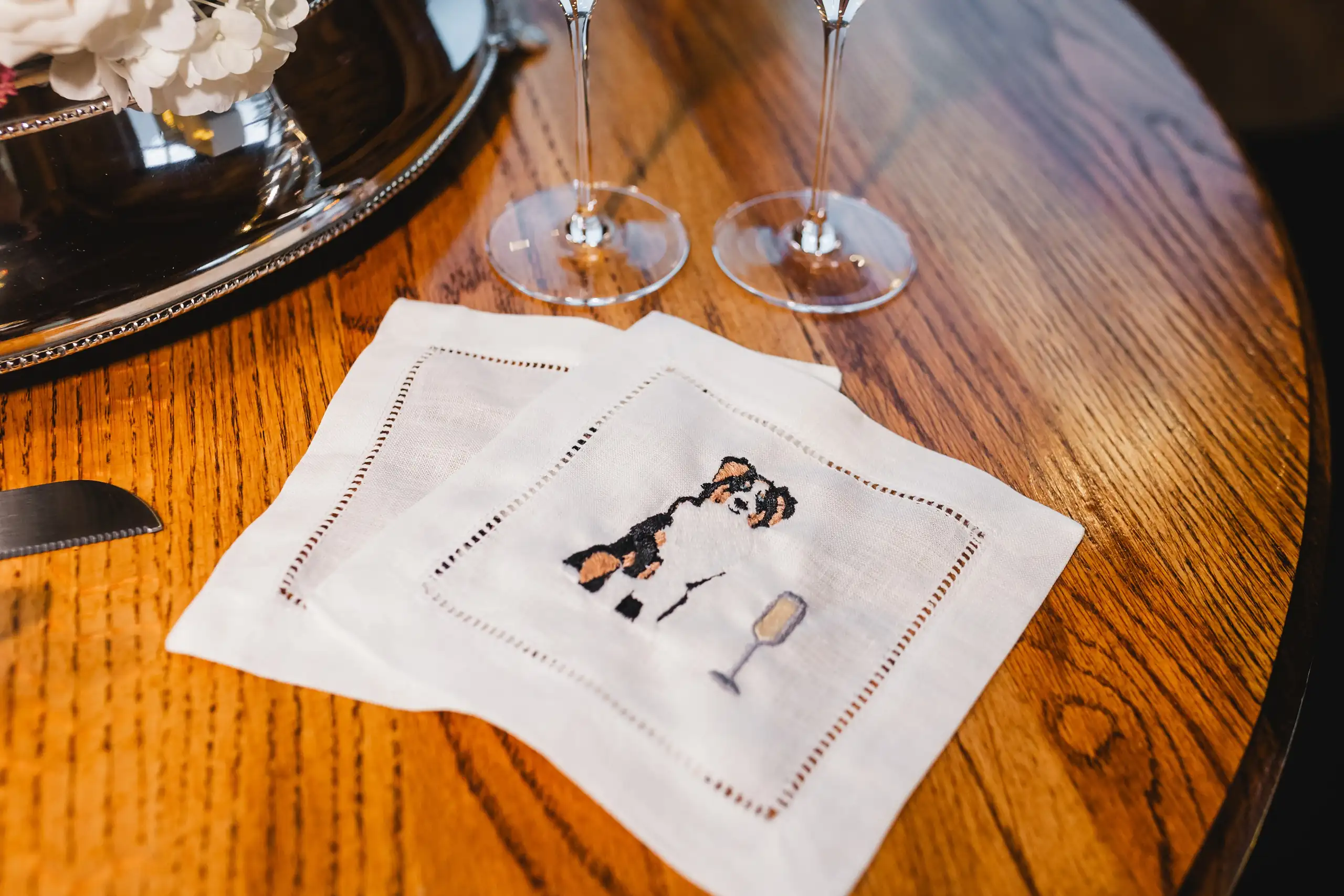 Reception Details: the embroidered cocktail napkins on the wooden table, at a wedding at The Venue at Sharp Mountain in Jasper, GA