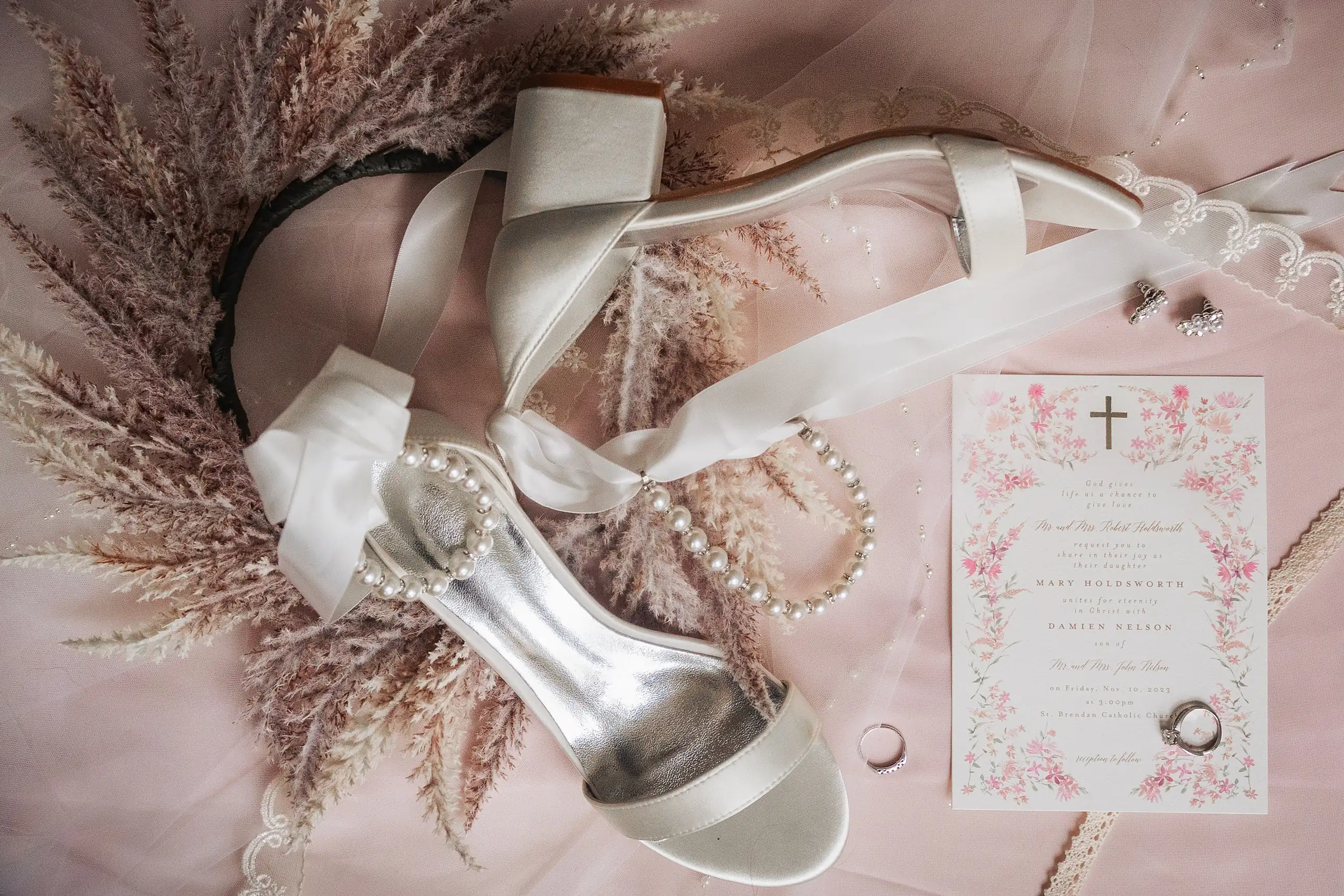 Wedding Details: her shoes, the invitation and the pampas, in a set, at a wedding at Swan Lake Overlook in Dawsonville, GA