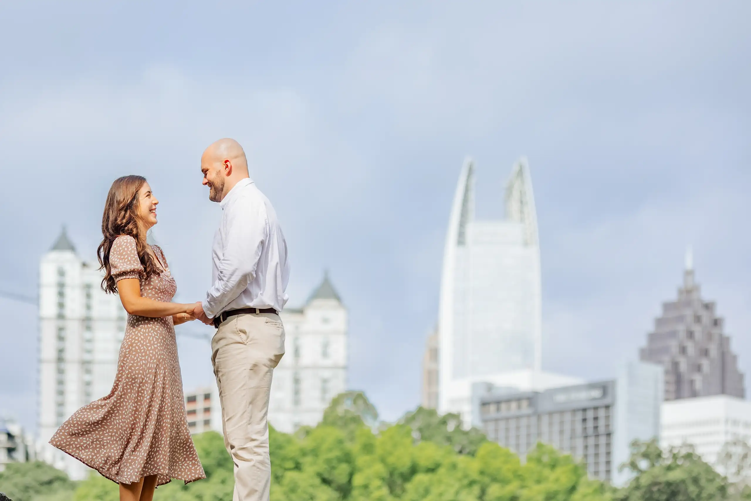 Engagement Portraits: the couple facing each other below the skyline, during their engagement session at Piedmont Park in Atlanta, GA