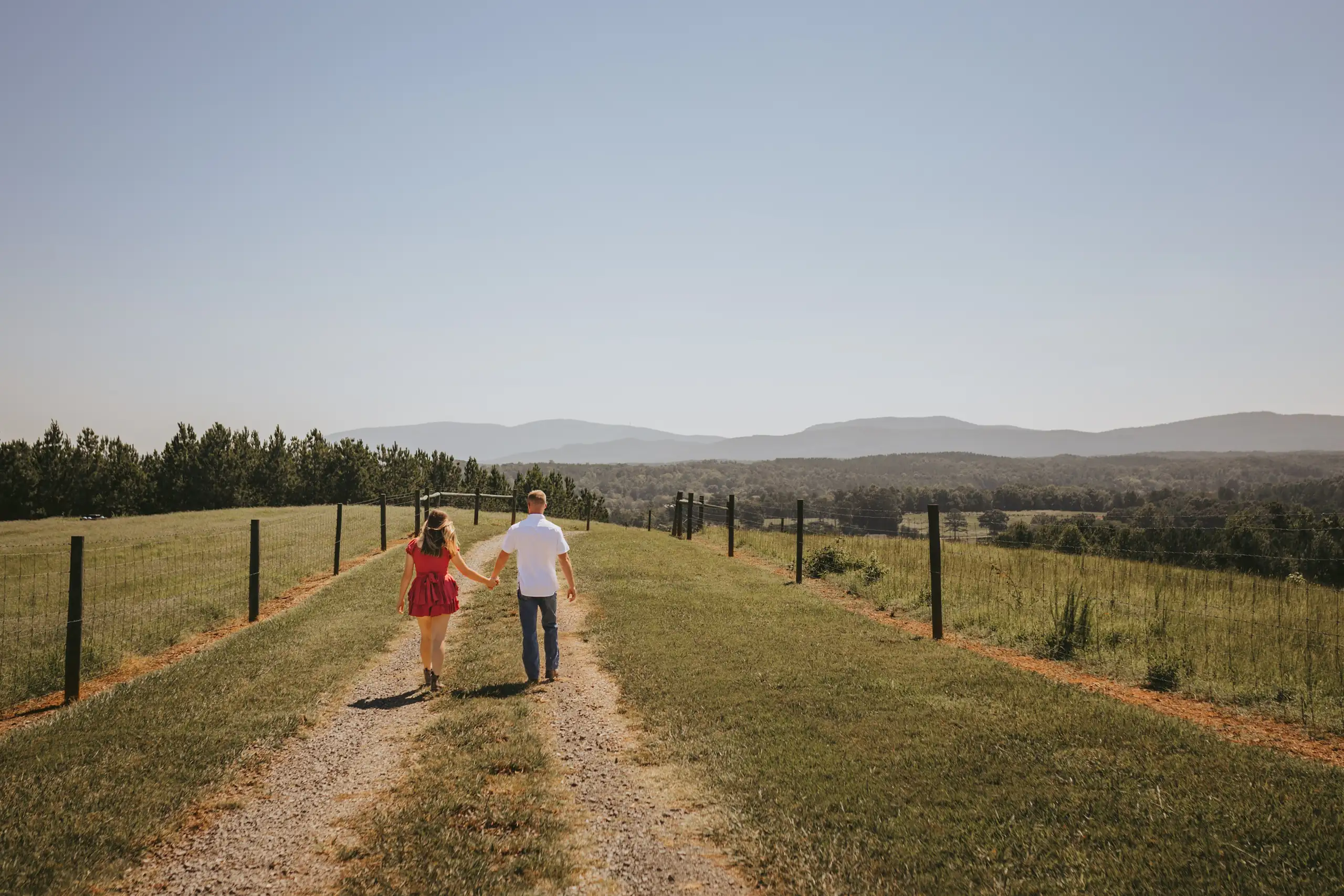 Engagement Portraits: the couple far down the fenced track, during their engagement session at a ranch in White, GA