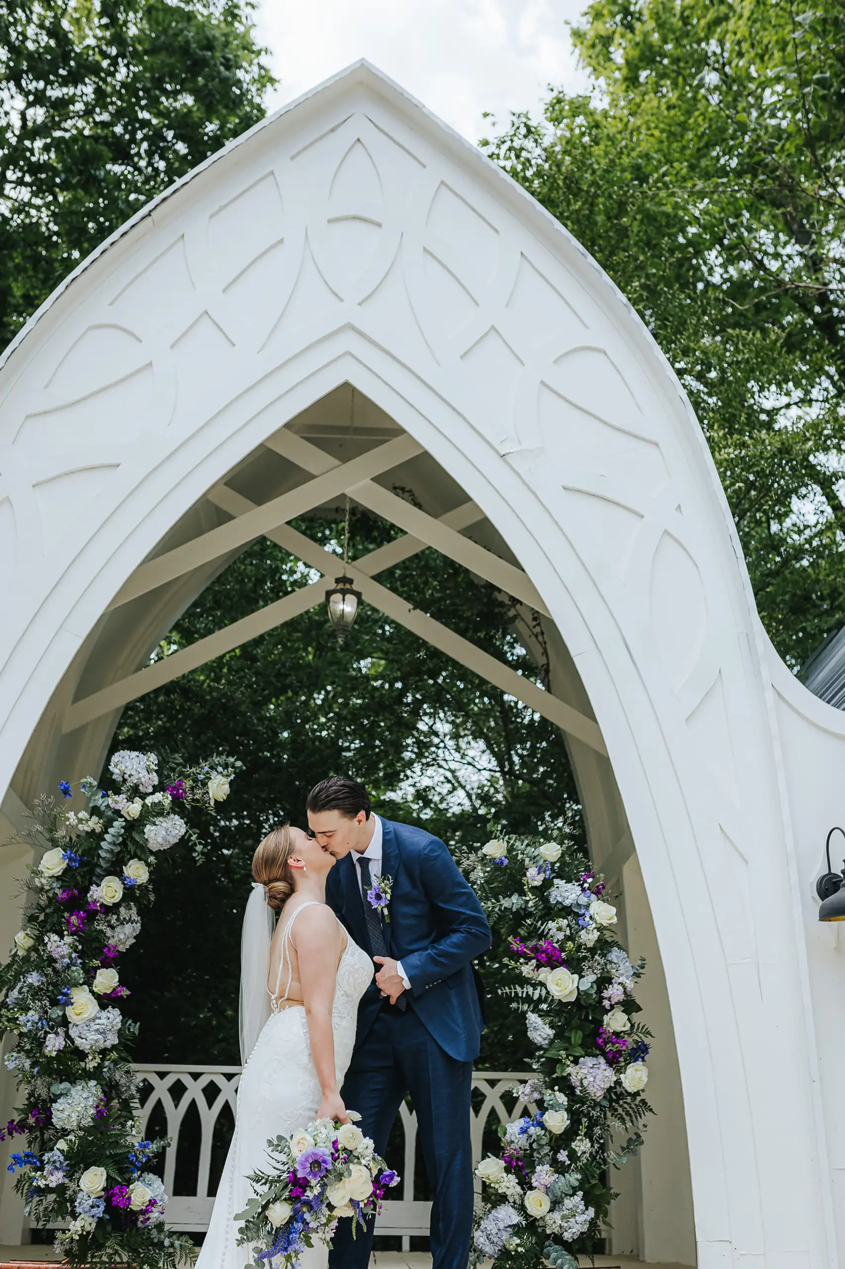 Wedding Formals: a kiss framed in the white gothic arch, at their wedding at the Wildflower 301 in Greensboro, GA