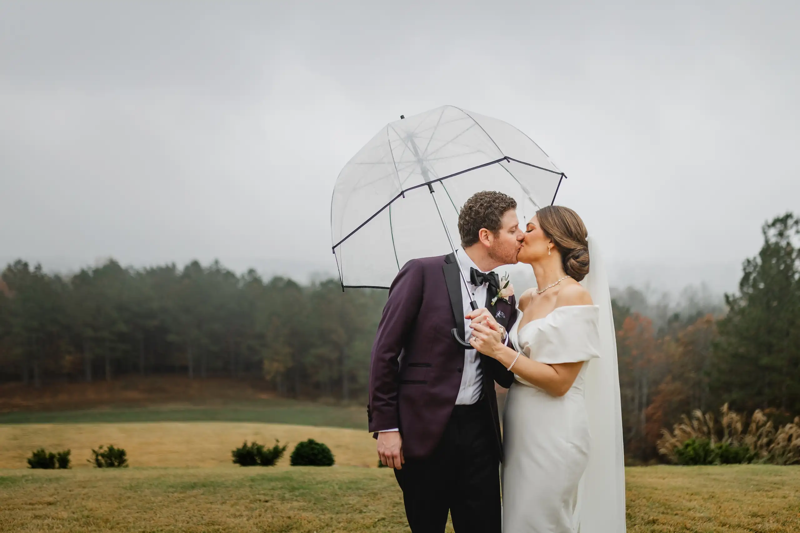 Wedding Formals: a kiss under the umbrella in the rain, at their wedding at The Venue at Sharp Mountain in Jasper, GA