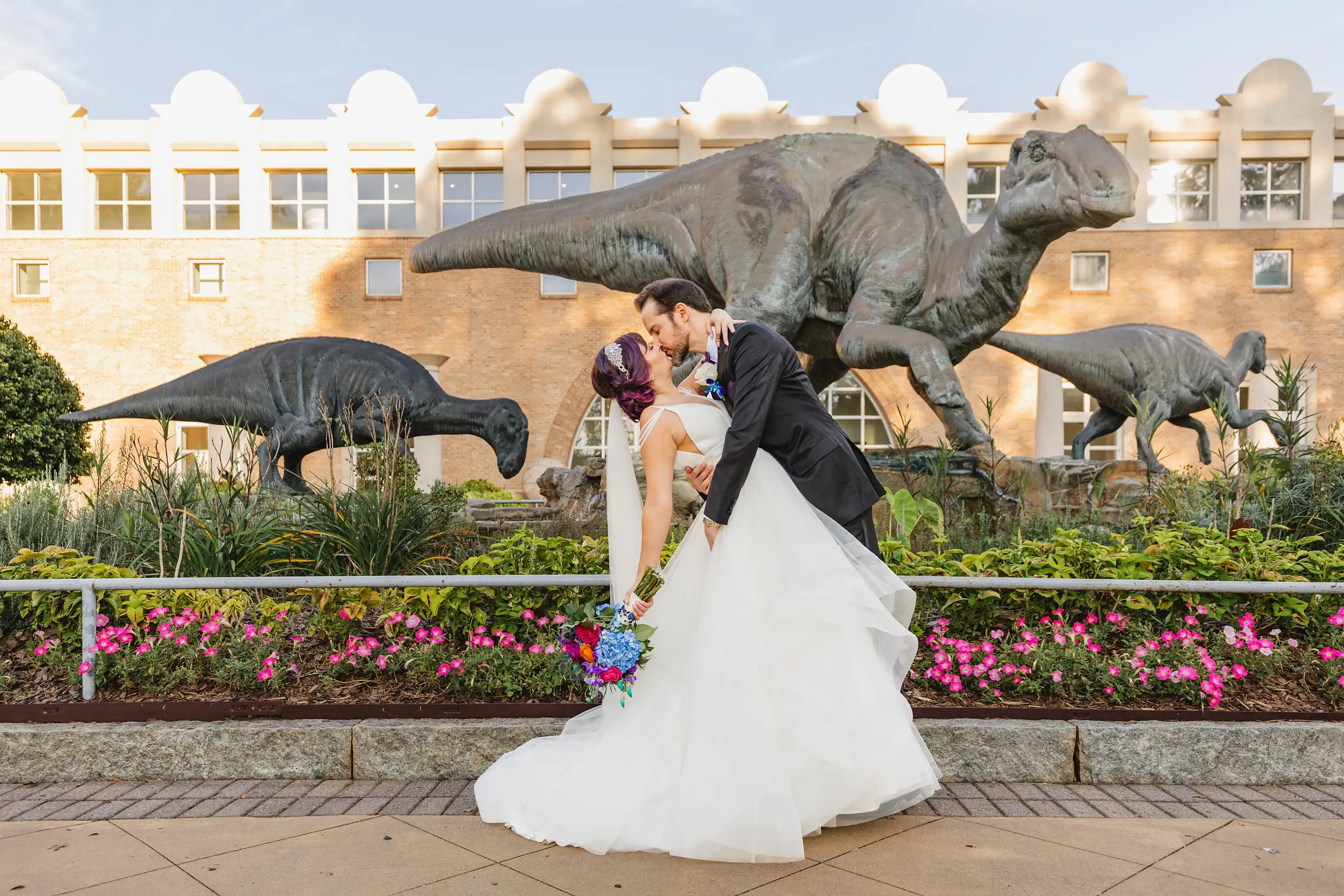 Wedding Formals: a dip kiss in front of the dinosaur statues, at their wedding at Fernbank Museum in Atlanta, GA