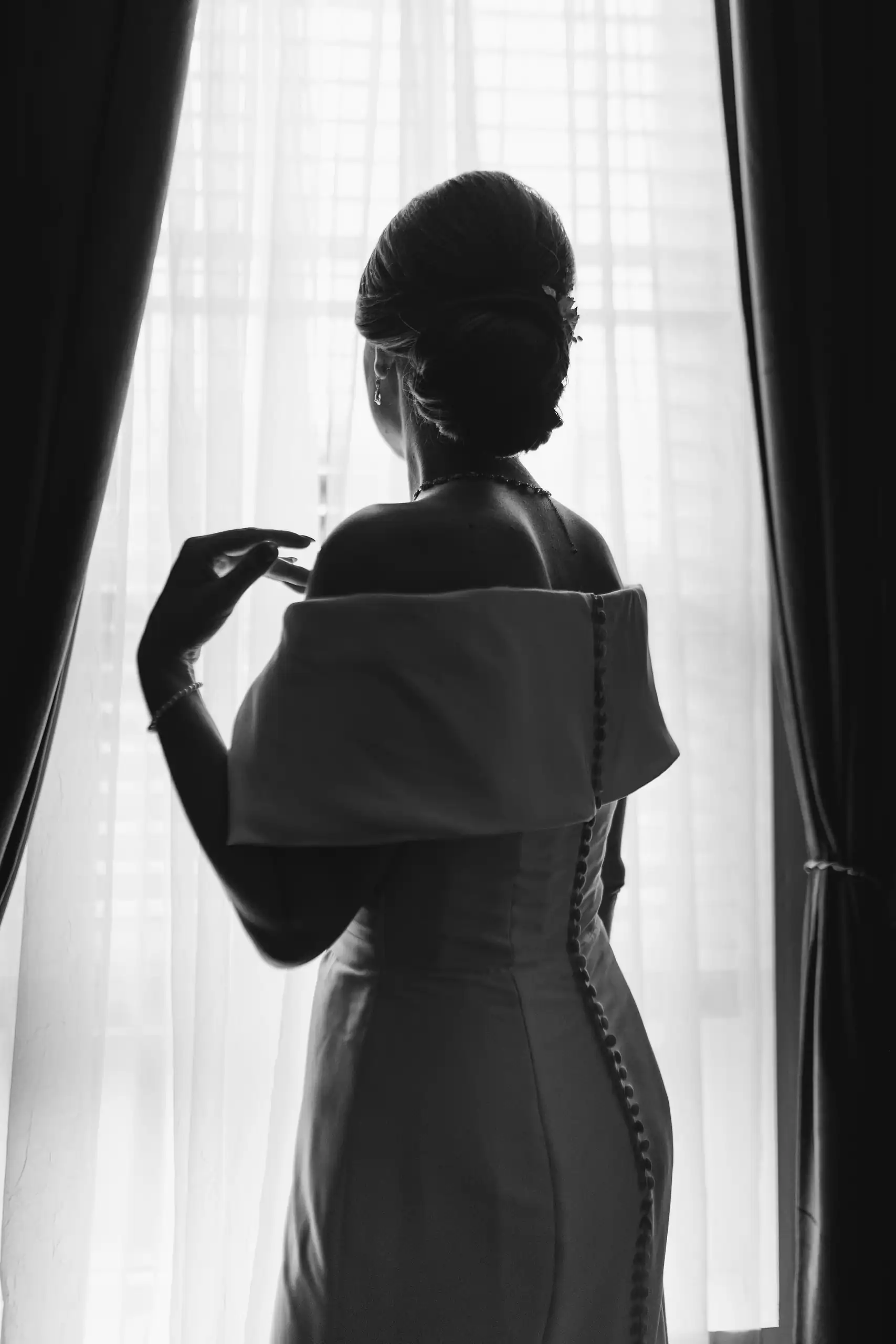 Getting Ready: the bride at the window in silhouette, in black and white, before their wedding at The Venue at Sharp Mountain in Jasper, GA