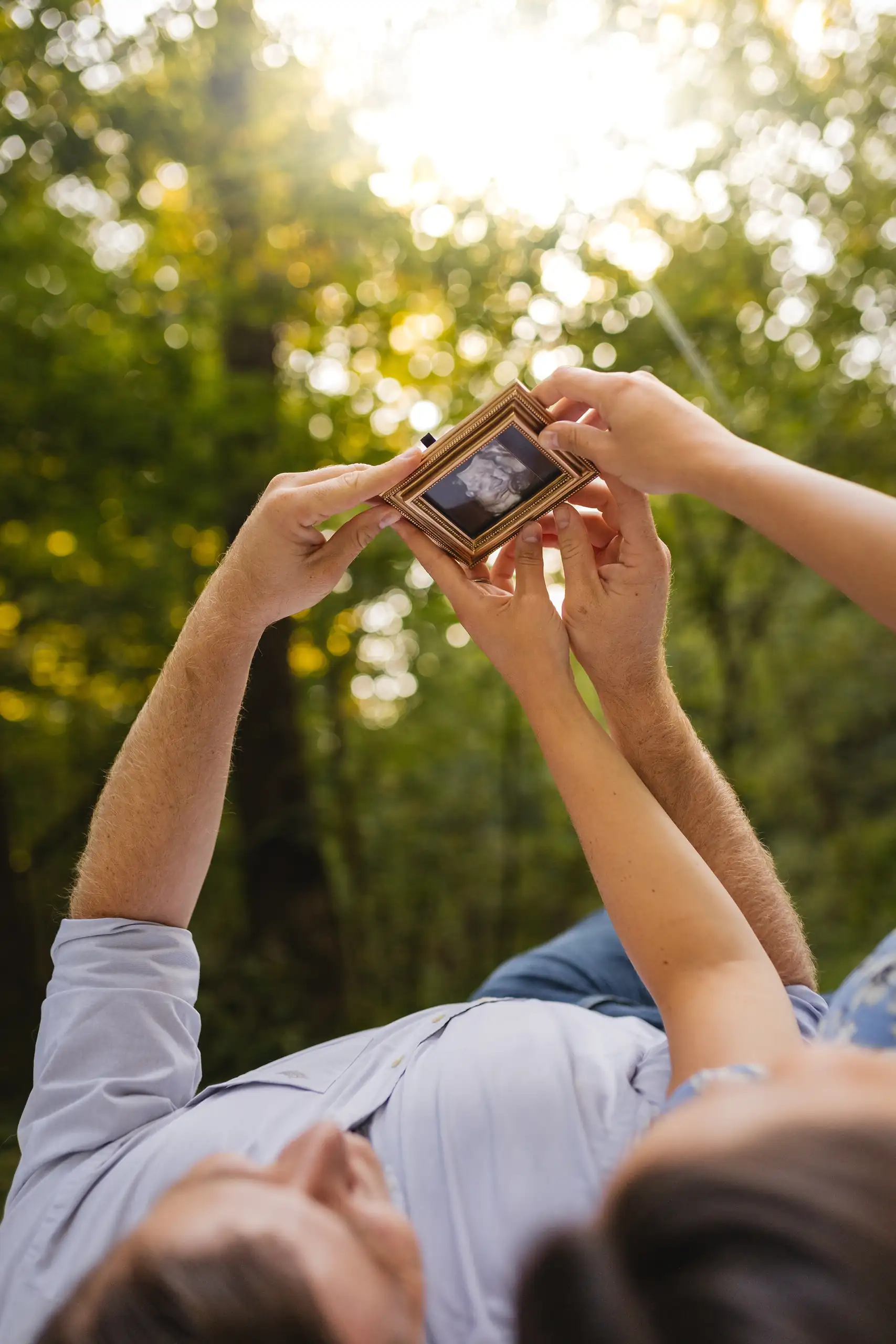 Maternity Portraits: the two of them lying in the grass, looking at the scan, at their maternity session in Ball Ground, GA