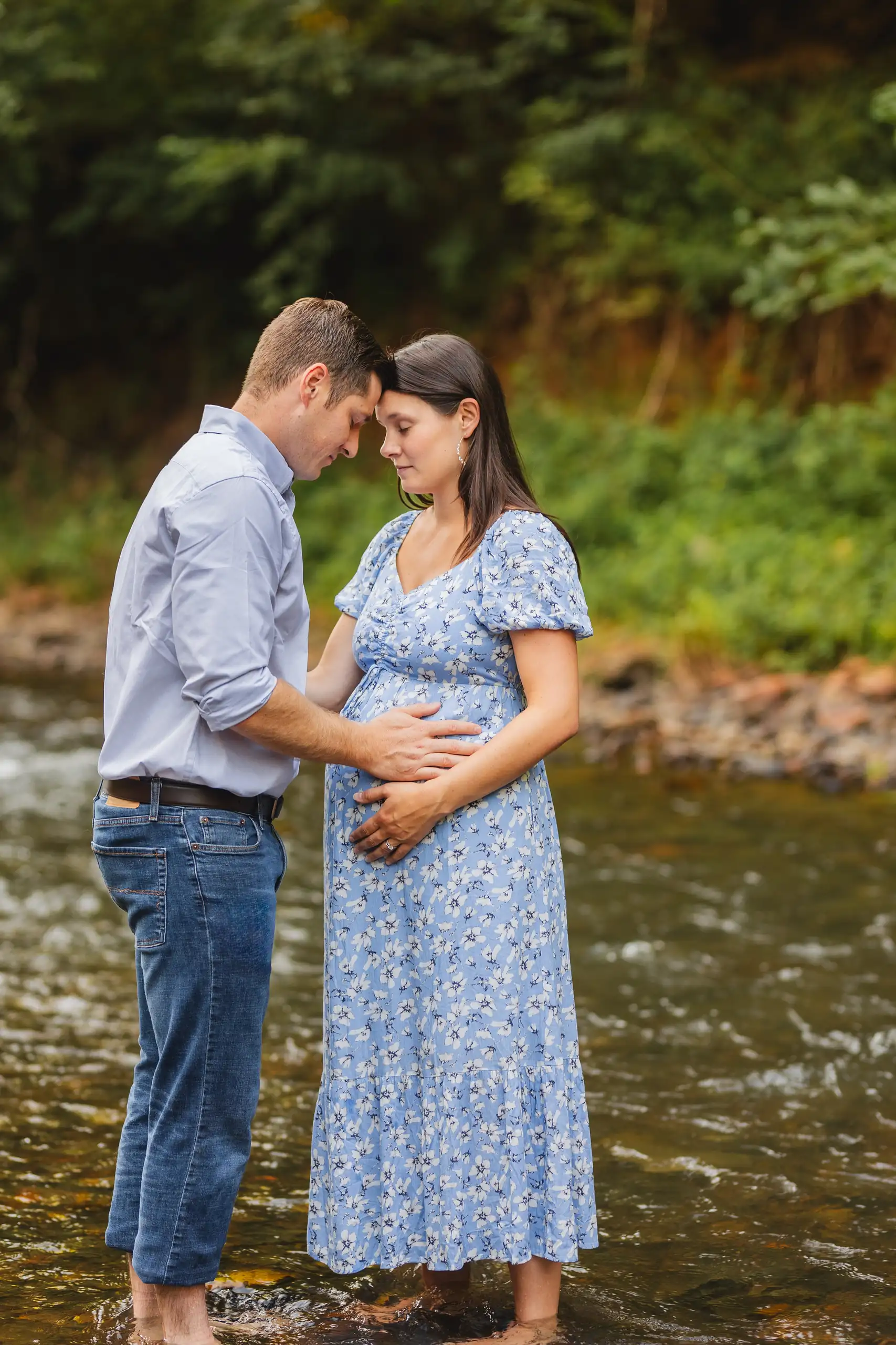 Maternity Portraits: the couple standing in the creek, his hands on the bump, at their maternity session in Ball Ground, GA