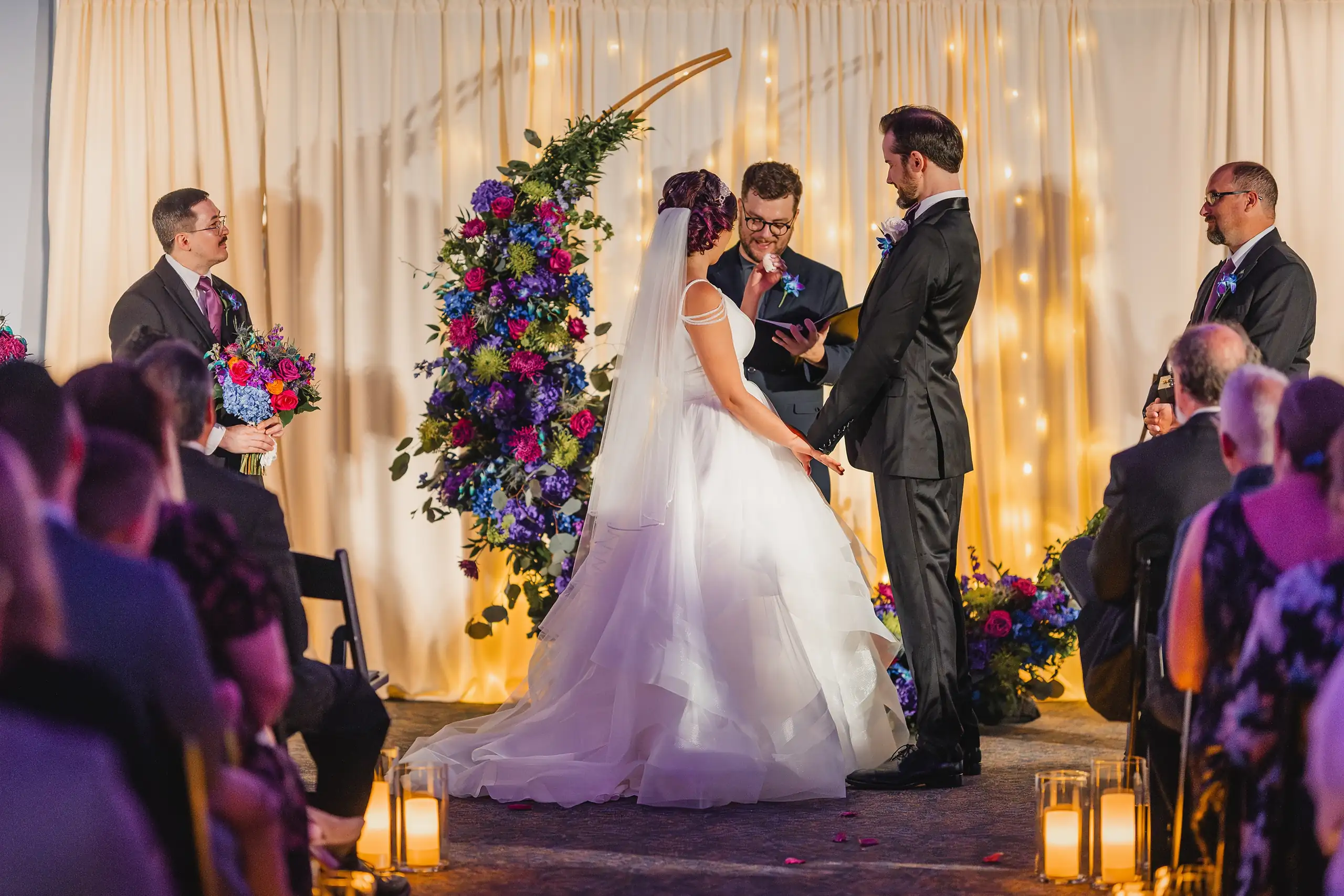 Wedding Ceremony: the vows at the flowered arch under the purple light, at their wedding at Fernbank Museum in Atlanta, GA