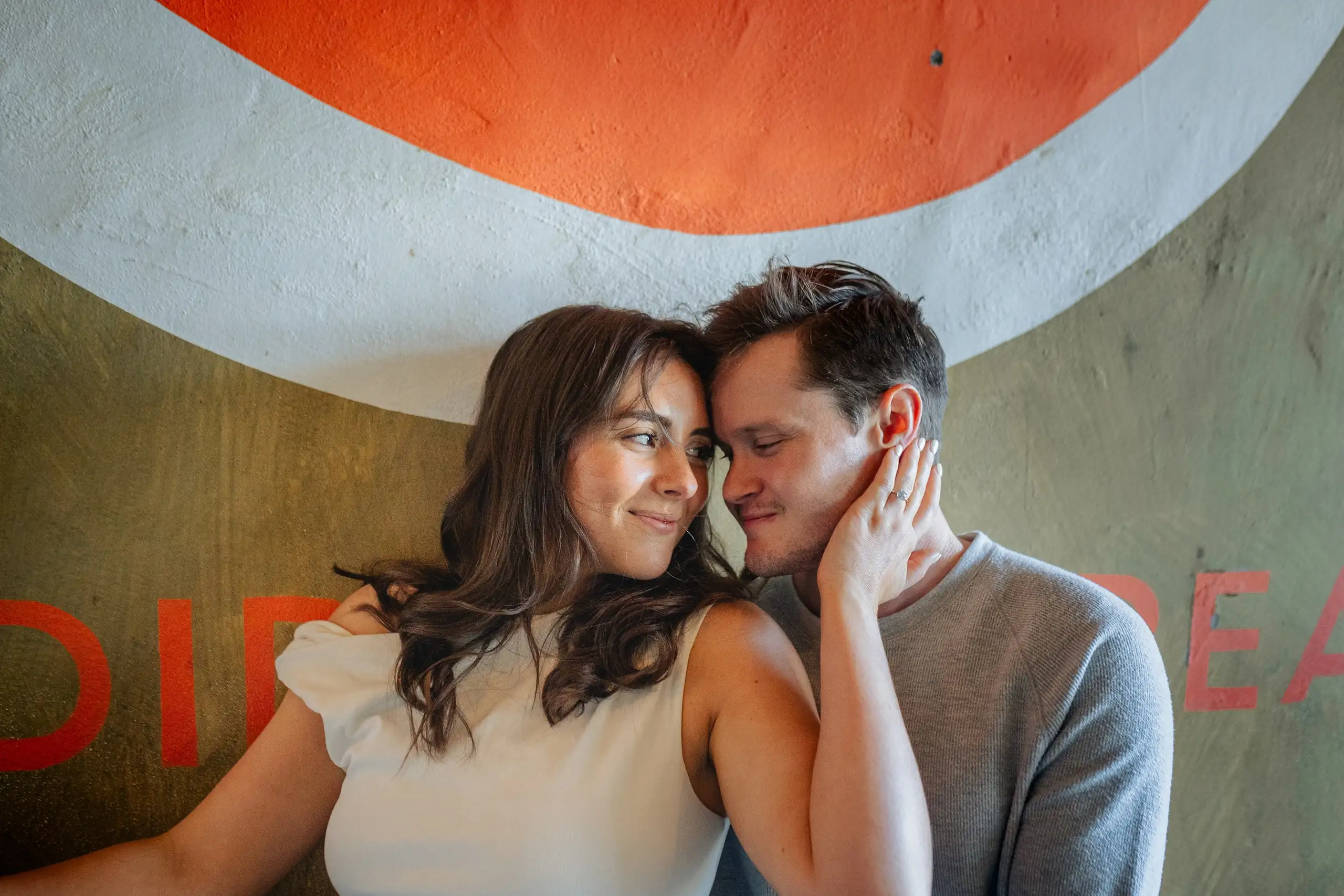 Engagement Portraits: her hand on his face against the painted wall, during their engagement session at Westside Provisions in Atlanta, GA