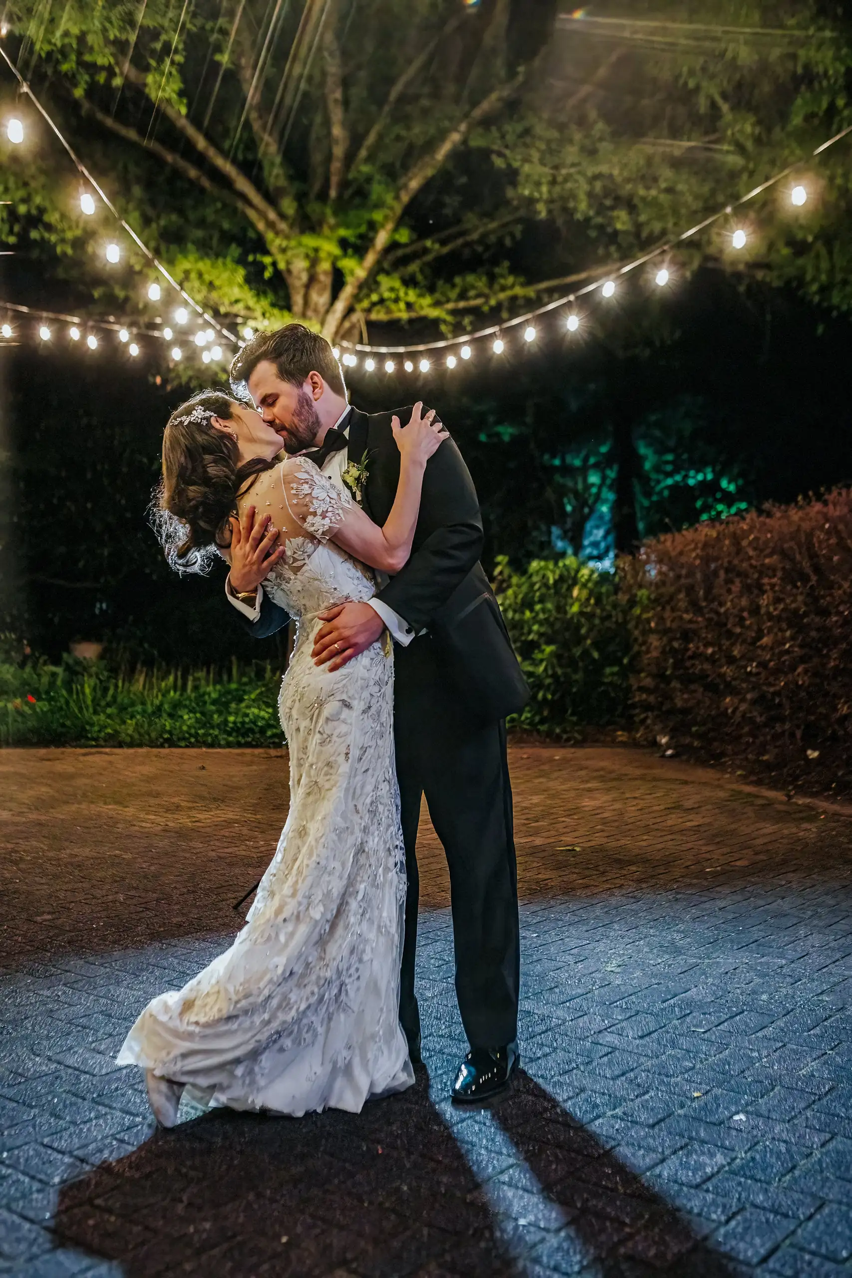 Wedding Formals: a kiss on the path under the strung lights, at their wedding at the Trolley Barn in Atlanta, GA
