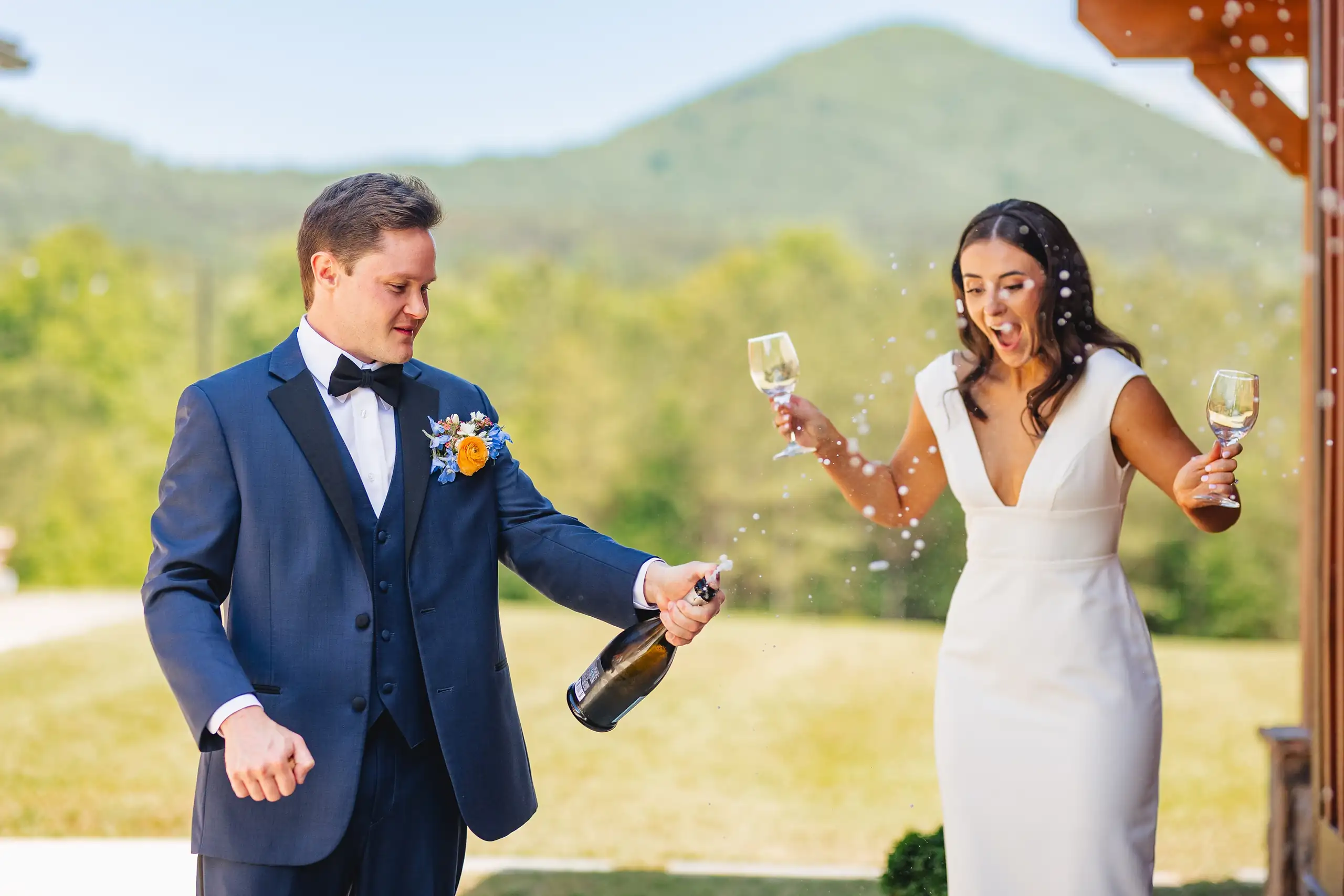 Wedding Reception: the groom opening champagne as she holds the glasses, at their wedding at The Venue at Sharp Mountain in Jasper, GA