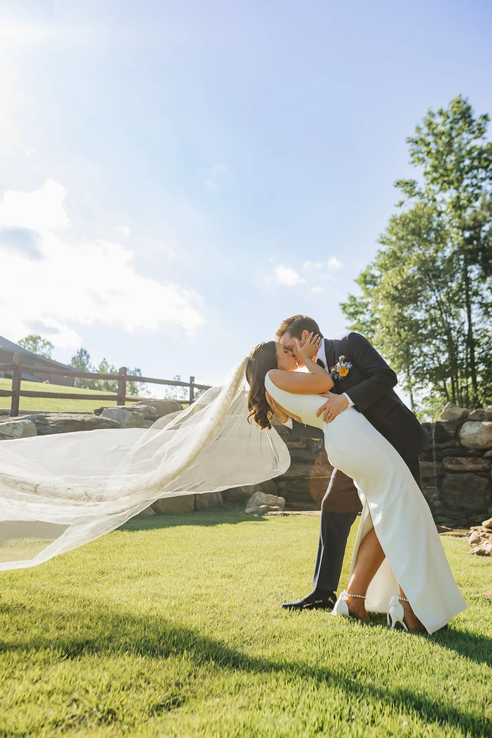 Wedding Formals: a kiss with her veil streaming across the grass, at their wedding at The Venue at Sharp Mountain in Jasper, GA