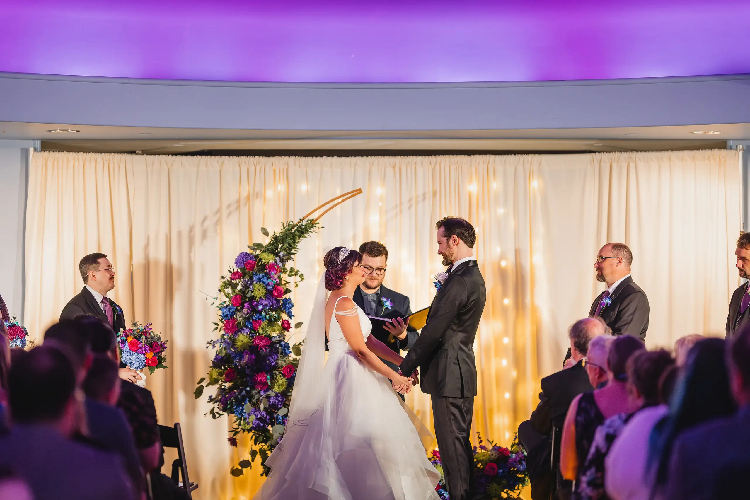 Wedding Ceremony: the vows said between the tall floral arrangements, at their wedding at Fernbank Museum in Atlanta, GA