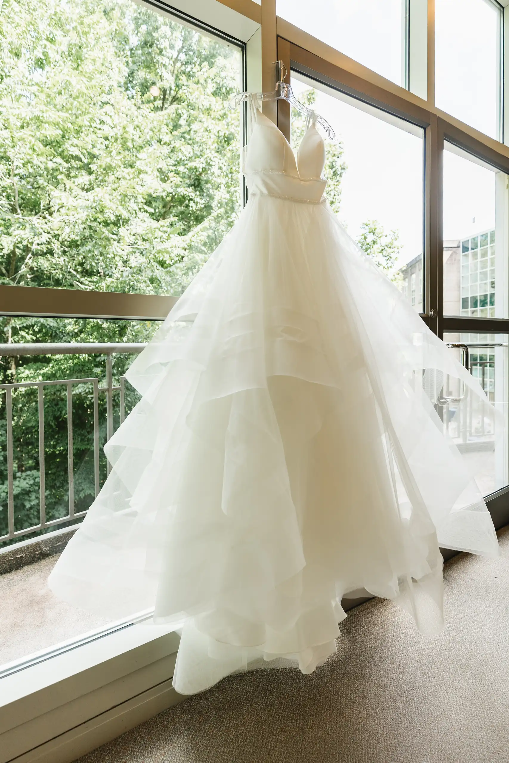 Wedding Details: the tiered gown hanging against the window, at a wedding at Fernbank Museum in Atlanta, GA