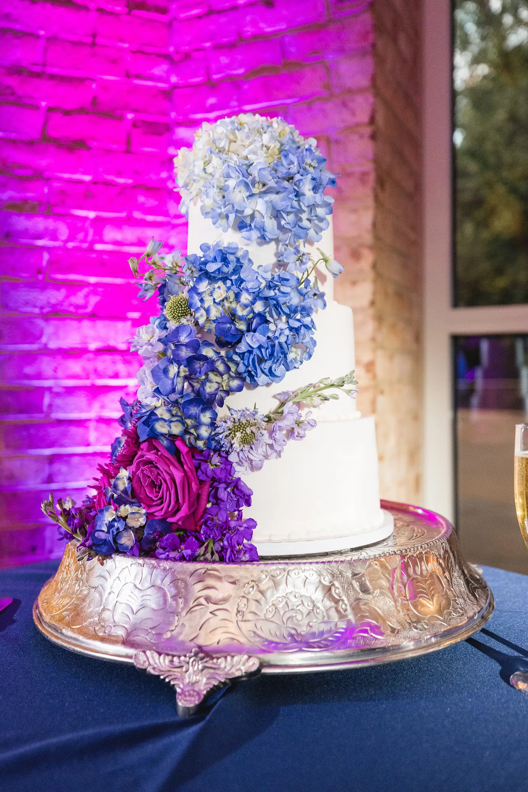 Wedding Cake Details: the cake dressed with blue and purple flowers, lit purple, at a wedding at Fernbank Museum in Atlanta, GA