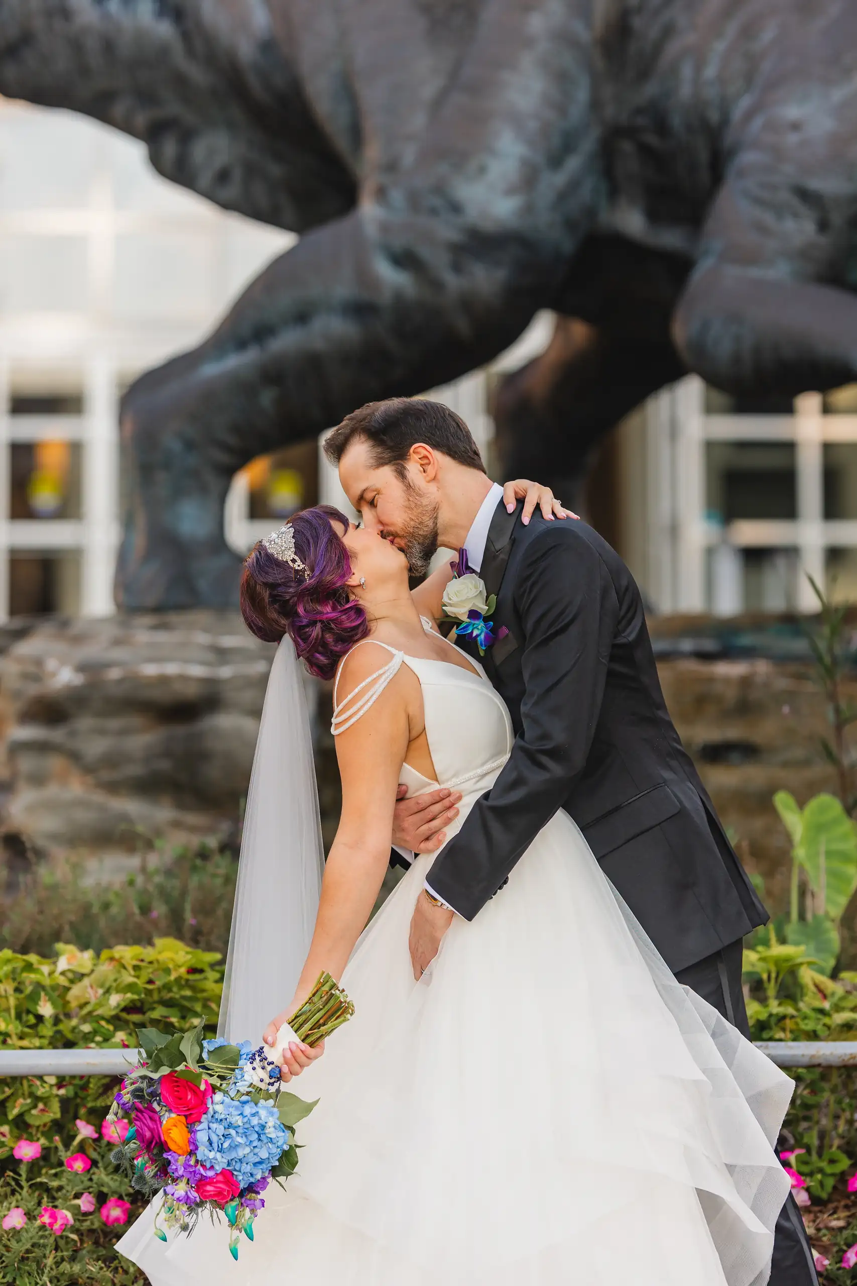 Wedding Formals: a kiss beneath the dinosaur statue in the garden, at their wedding at Fernbank Museum in Atlanta, GA