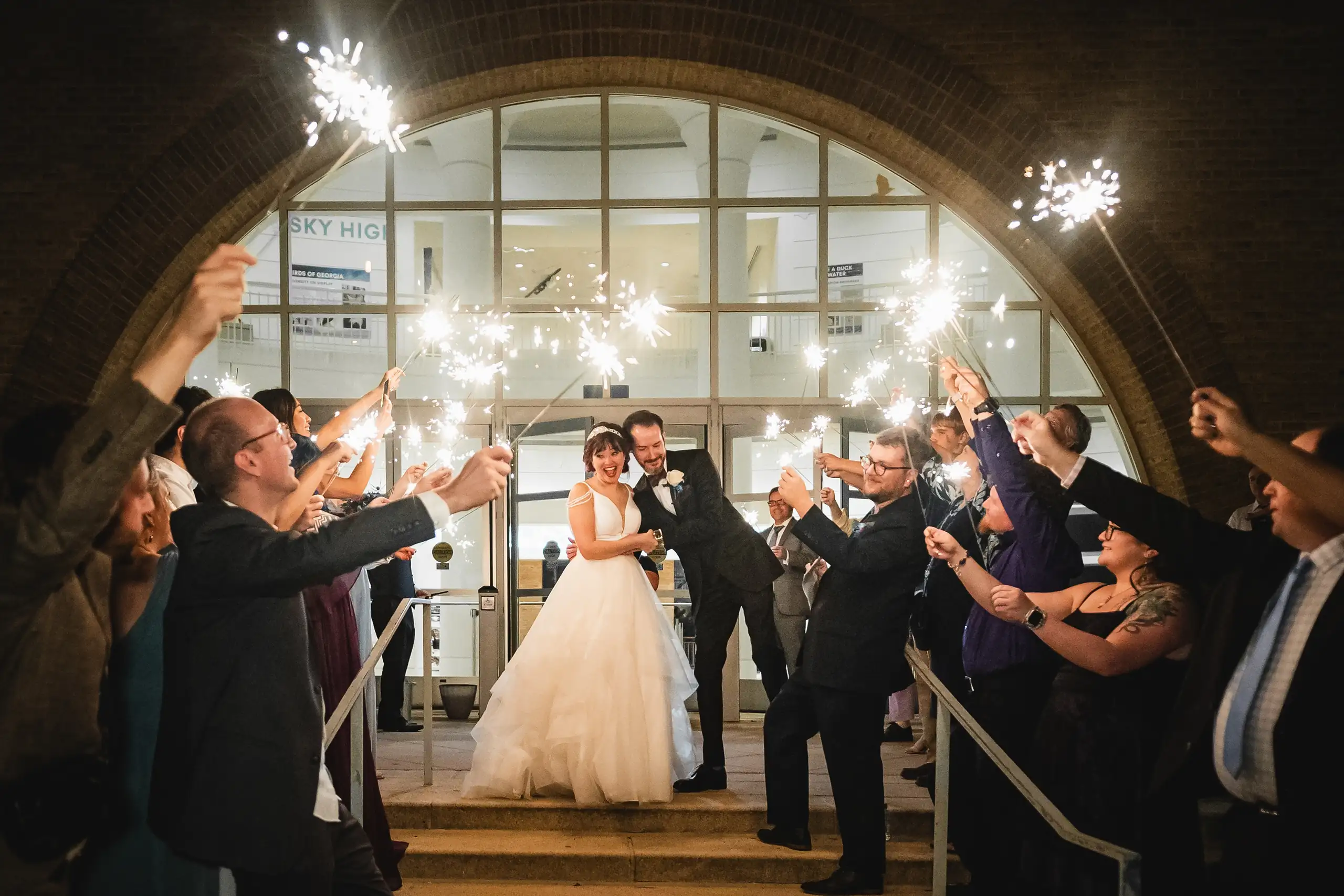 Sparkler Exit: the two of them under the brick arch, sparklers either side, at their wedding at Fernbank Museum in Atlanta, GA