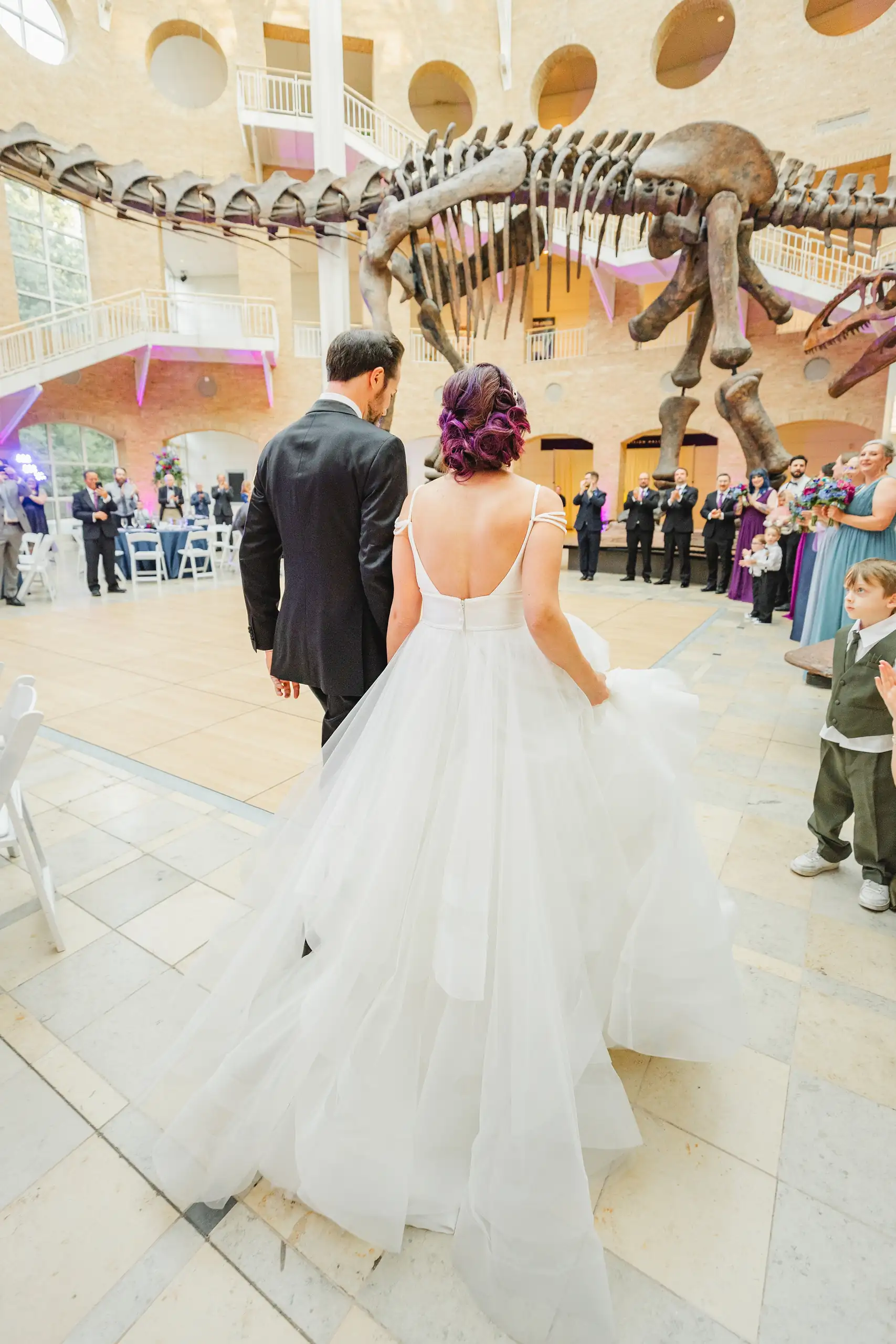 Wedding Reception: the couple walking in beneath the dinosaur skeleton, at their wedding at Fernbank Museum in Atlanta, GA