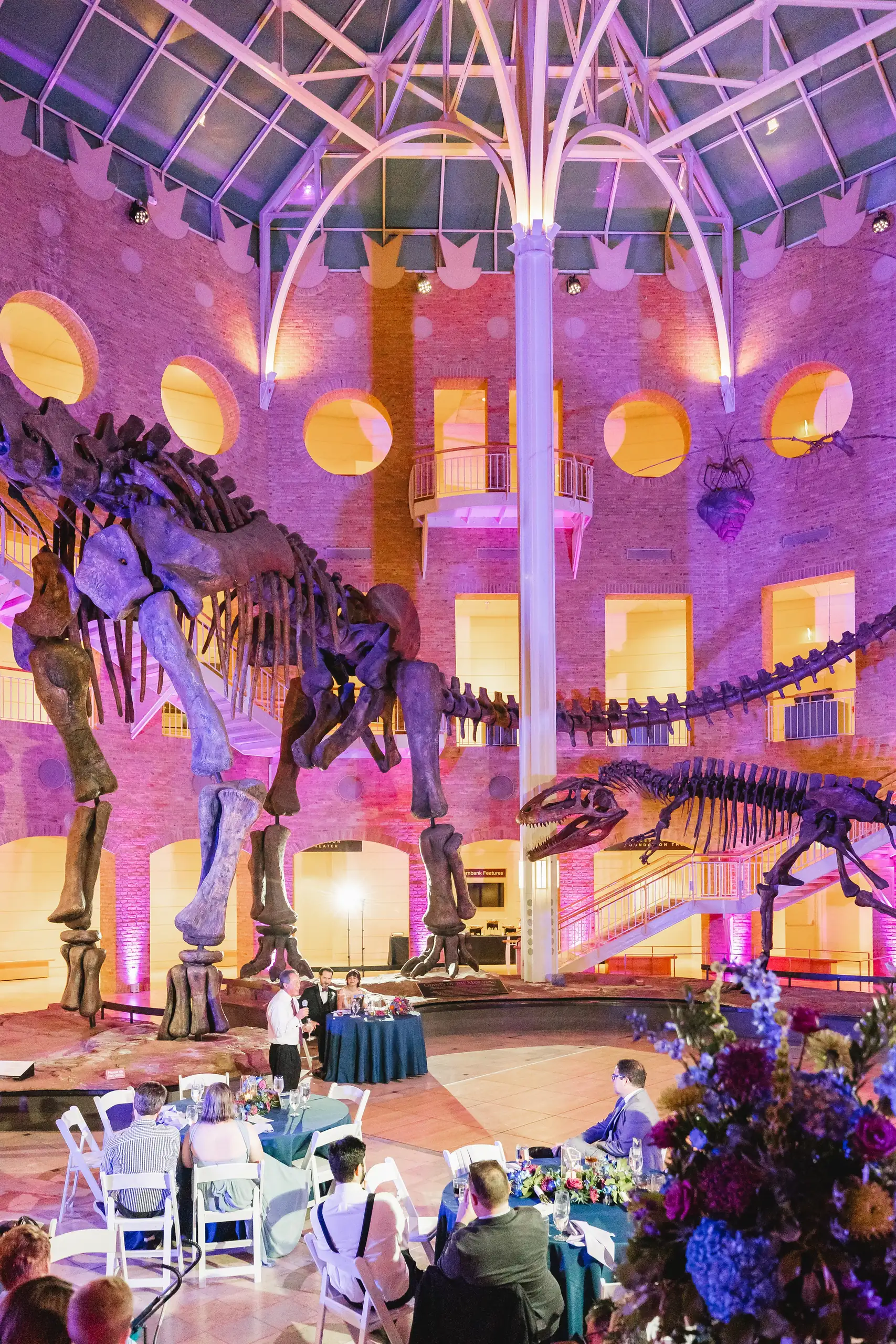 Wedding Reception: the Great Hall lit purple, the tables around the floor, at their wedding at Fernbank Museum in Atlanta, GA
