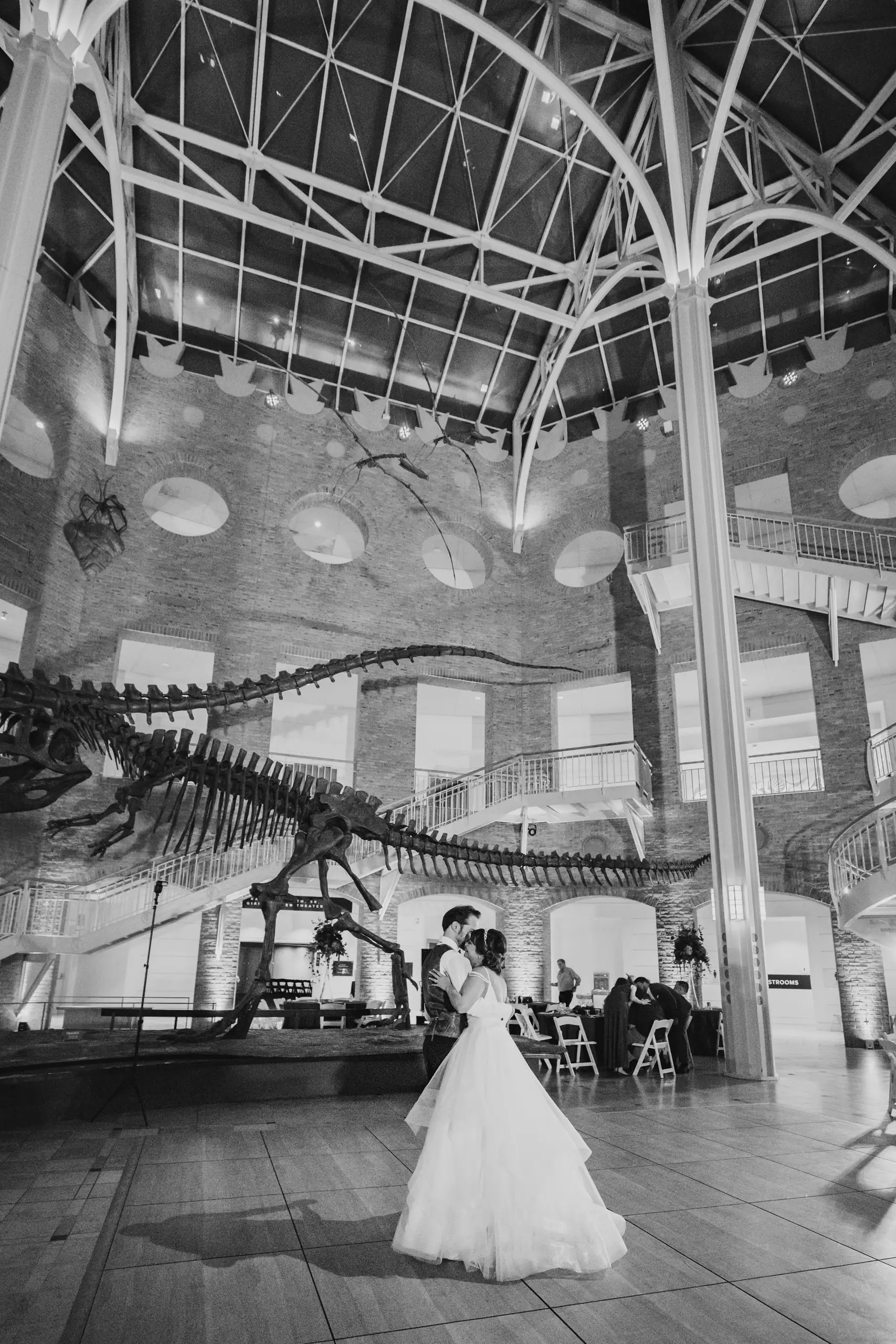 Wedding Reception: the bride dancing alone under the skeleton, in black and white, at their wedding at Fernbank Museum in Atlanta, GA