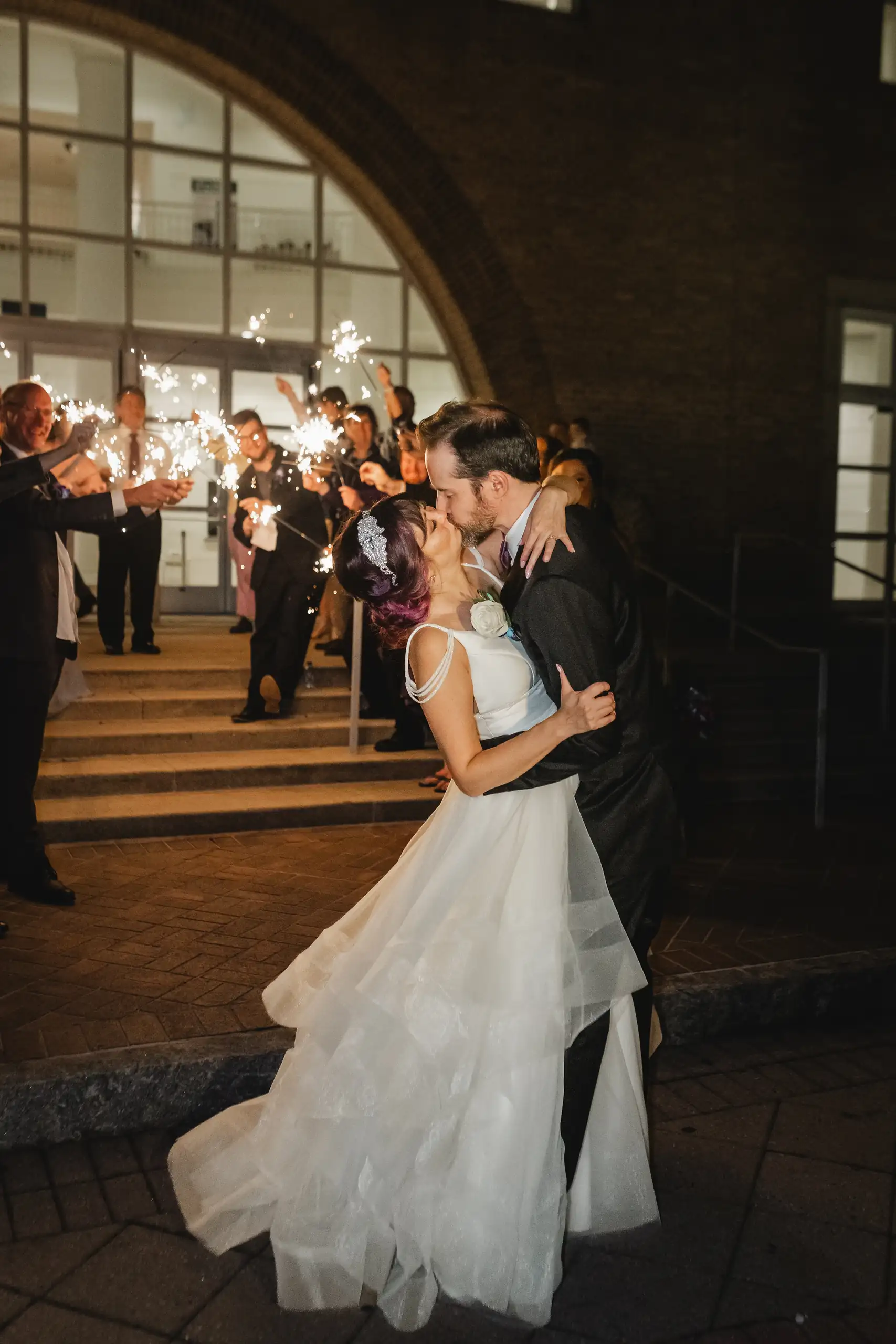 Sparkler Exit: a kiss in the doorway as the sparklers burn, at their wedding at Fernbank Museum in Atlanta, GA