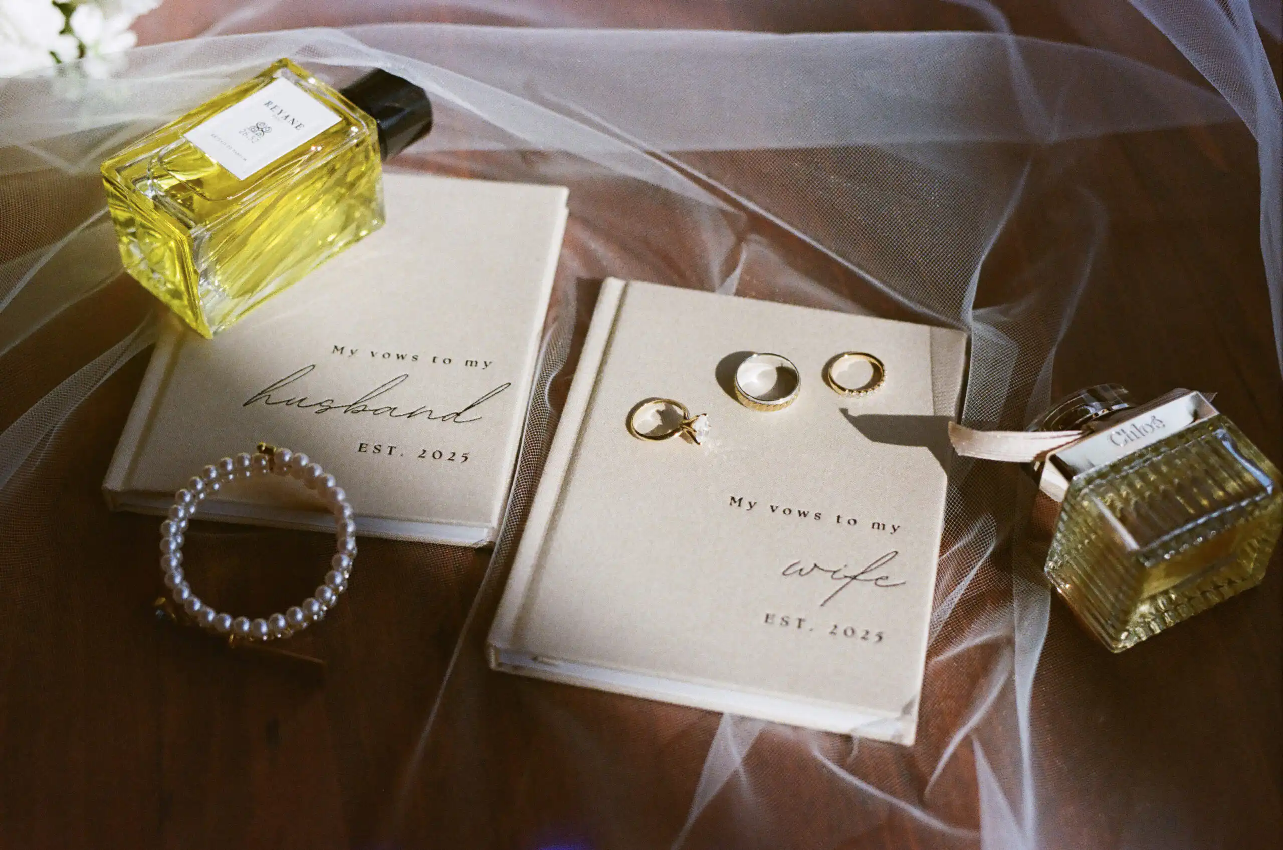 Vow books, rings, a pearl bracelet and perfume laid out before a wedding, shot on 35mm film