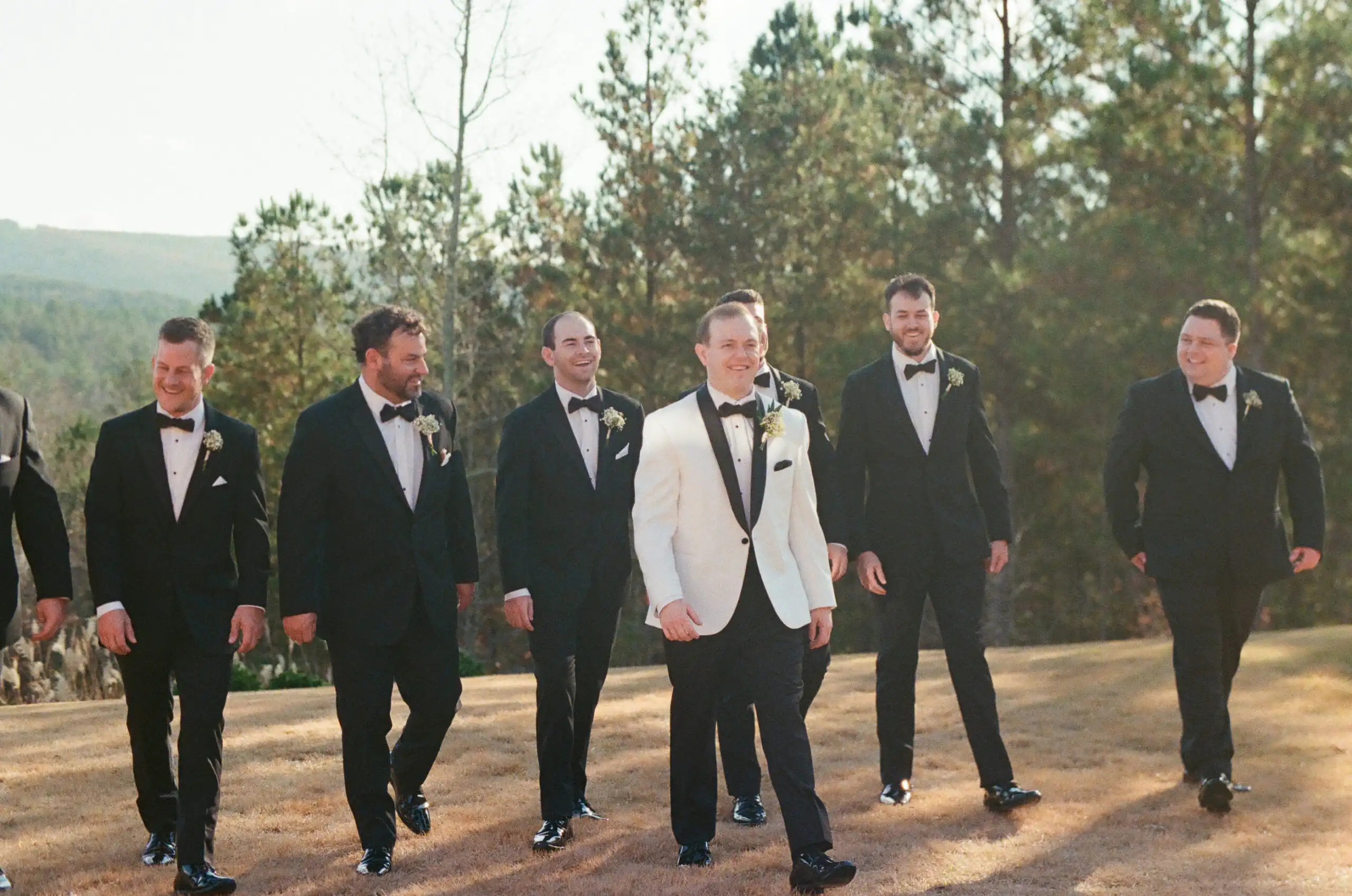Groom in a white dinner jacket walking with his groomsmen at their wedding, shot on 35mm film