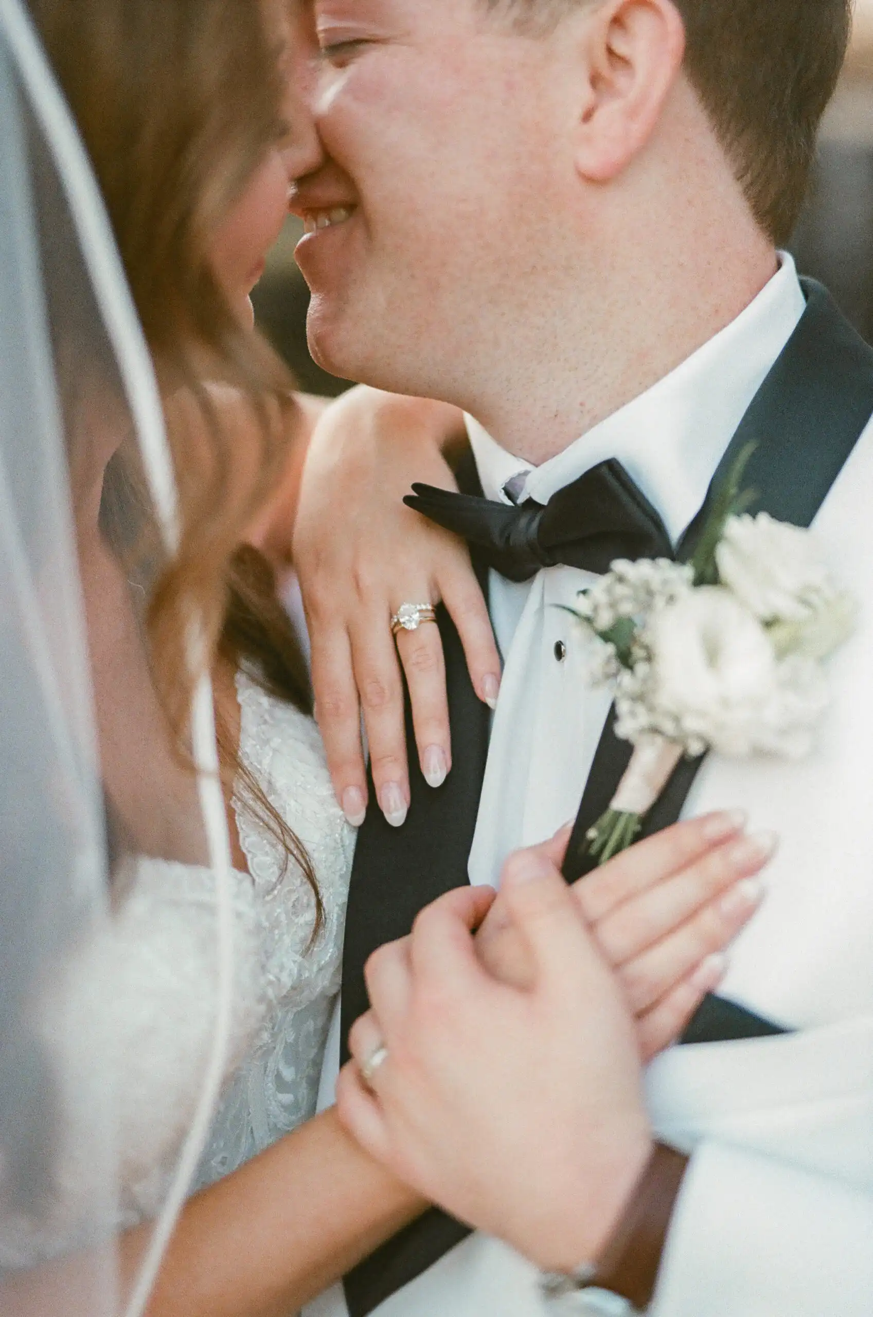 Bride's hands on the groom's chest at their wedding, with her ring and his boutonniere, shot on 35mm film