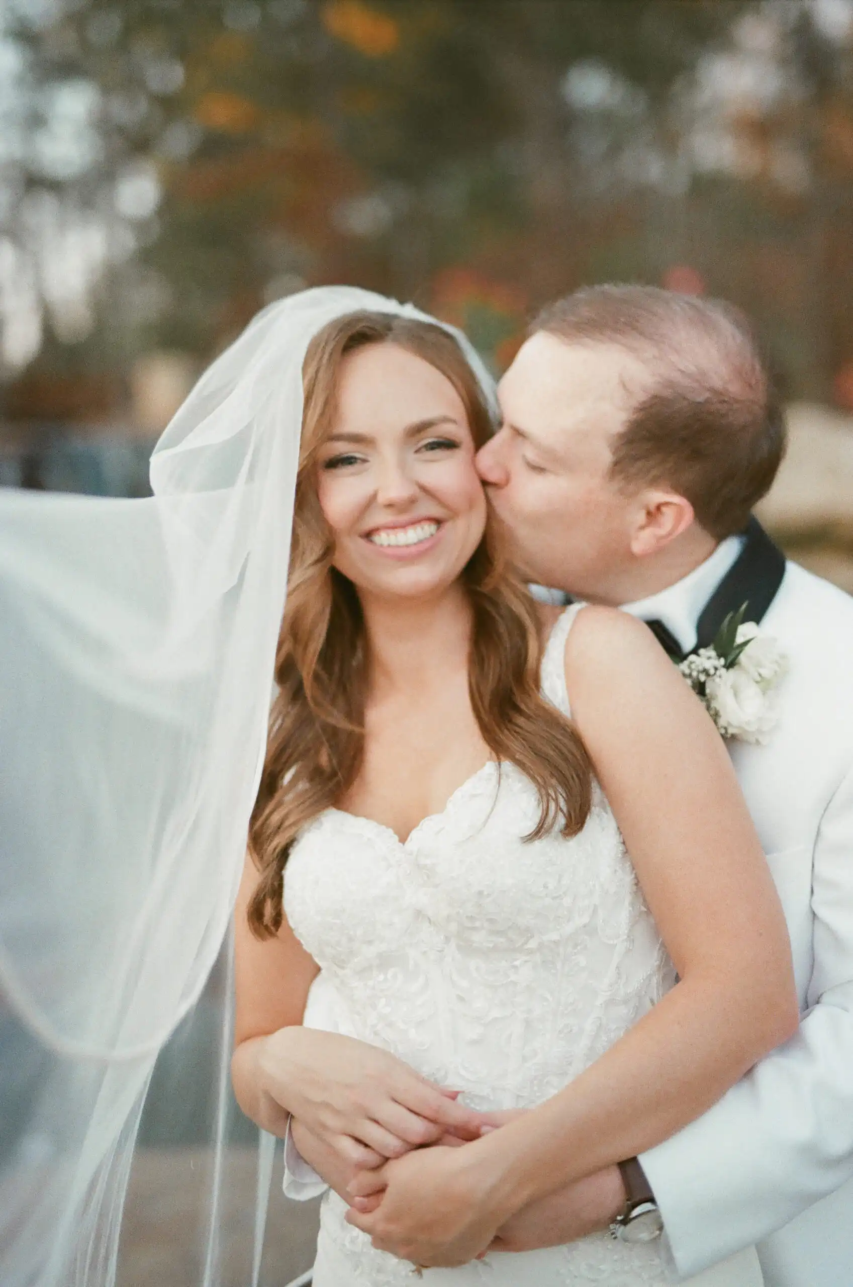 Groom kissing the bride's cheek beneath her veil at their wedding, shot on 35mm film