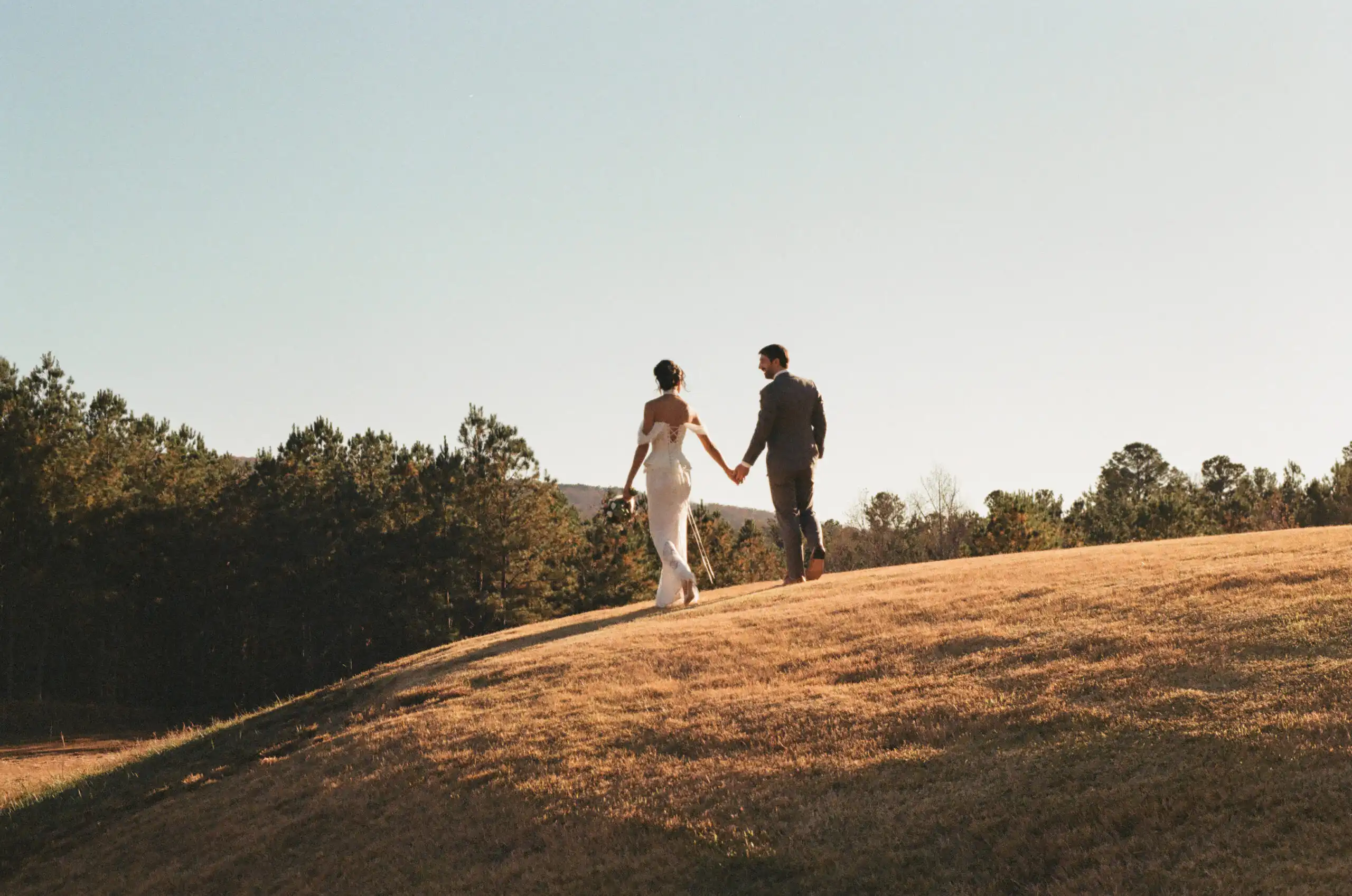 Bride and groom walking a grassy hill at their wedding, shot on 35mm film