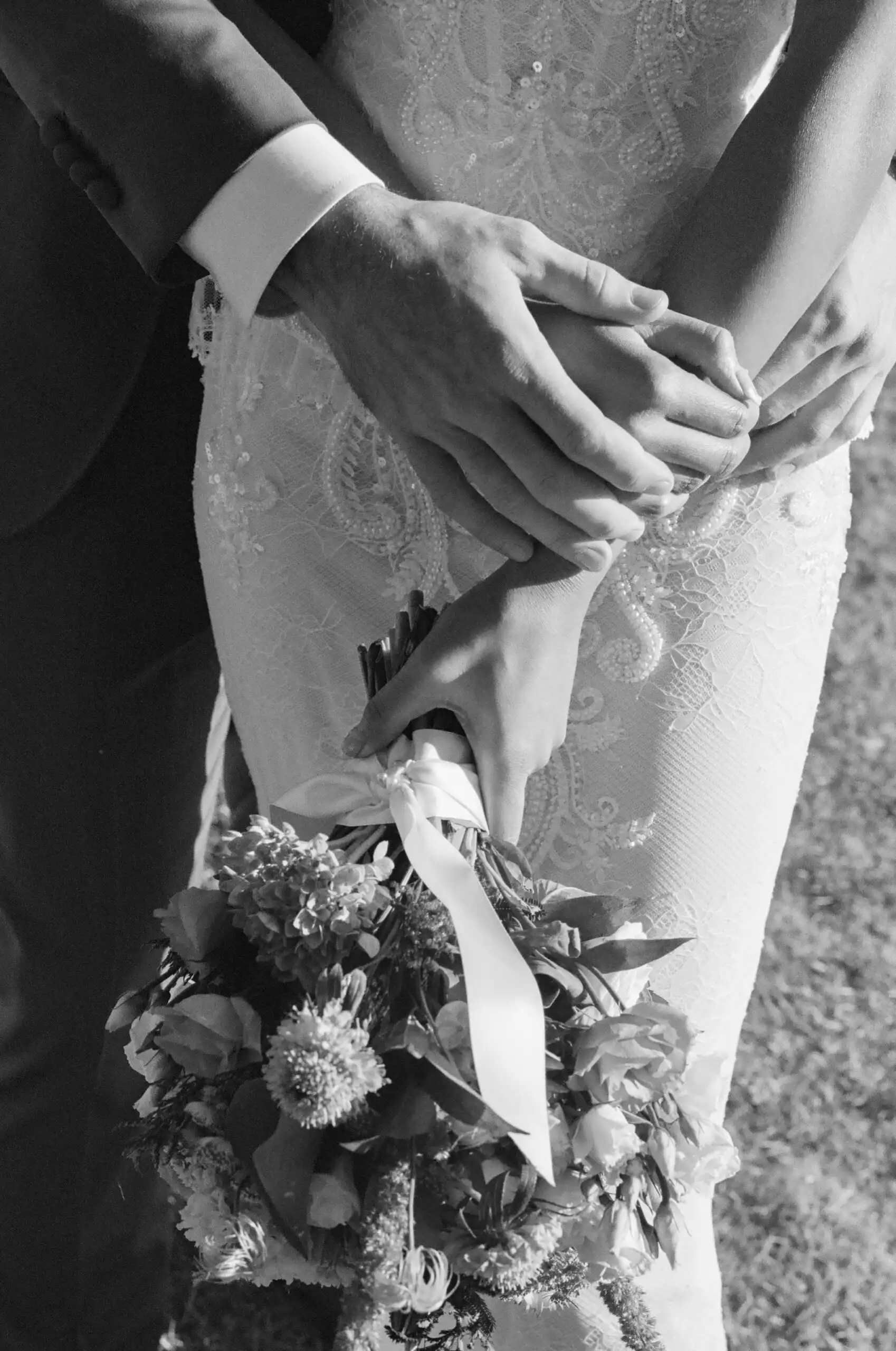 Groom's hands over the bride's above her wedding bouquet, in black and white on 35mm film