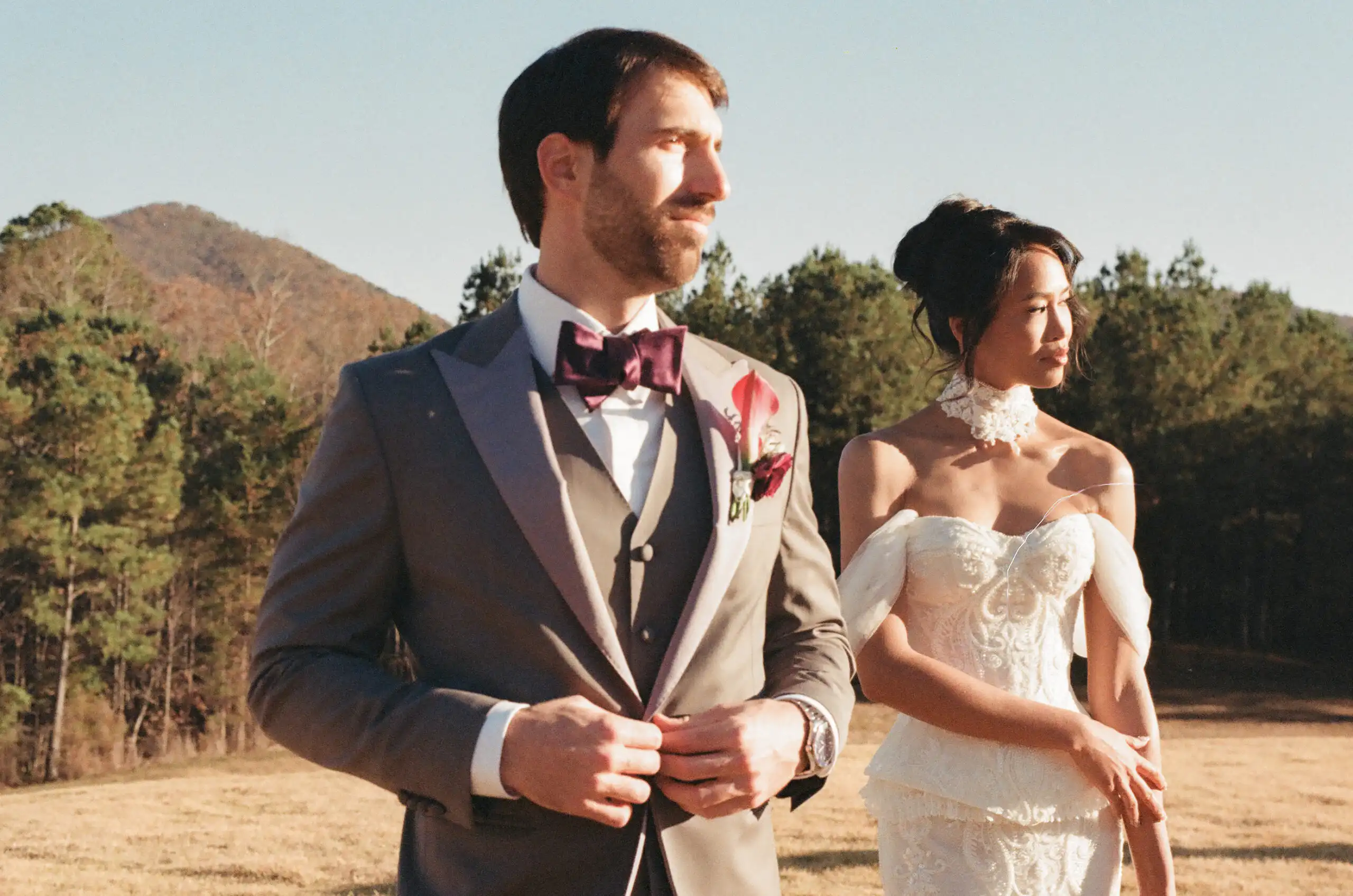 Groom buttoning his jacket with the bride behind him at their wedding, shot on 35mm film