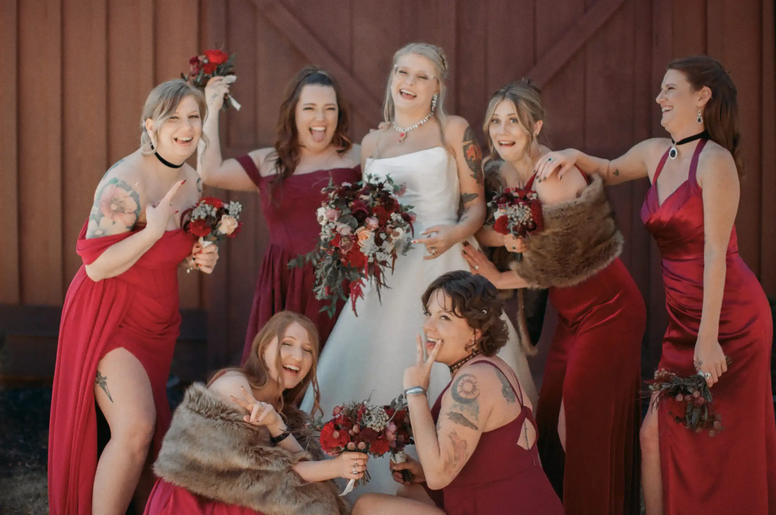 Bride and her bridesmaids in red by the barn door at their wedding, shot on 35mm film at The Venue at Sharp Mountain in North Georgia