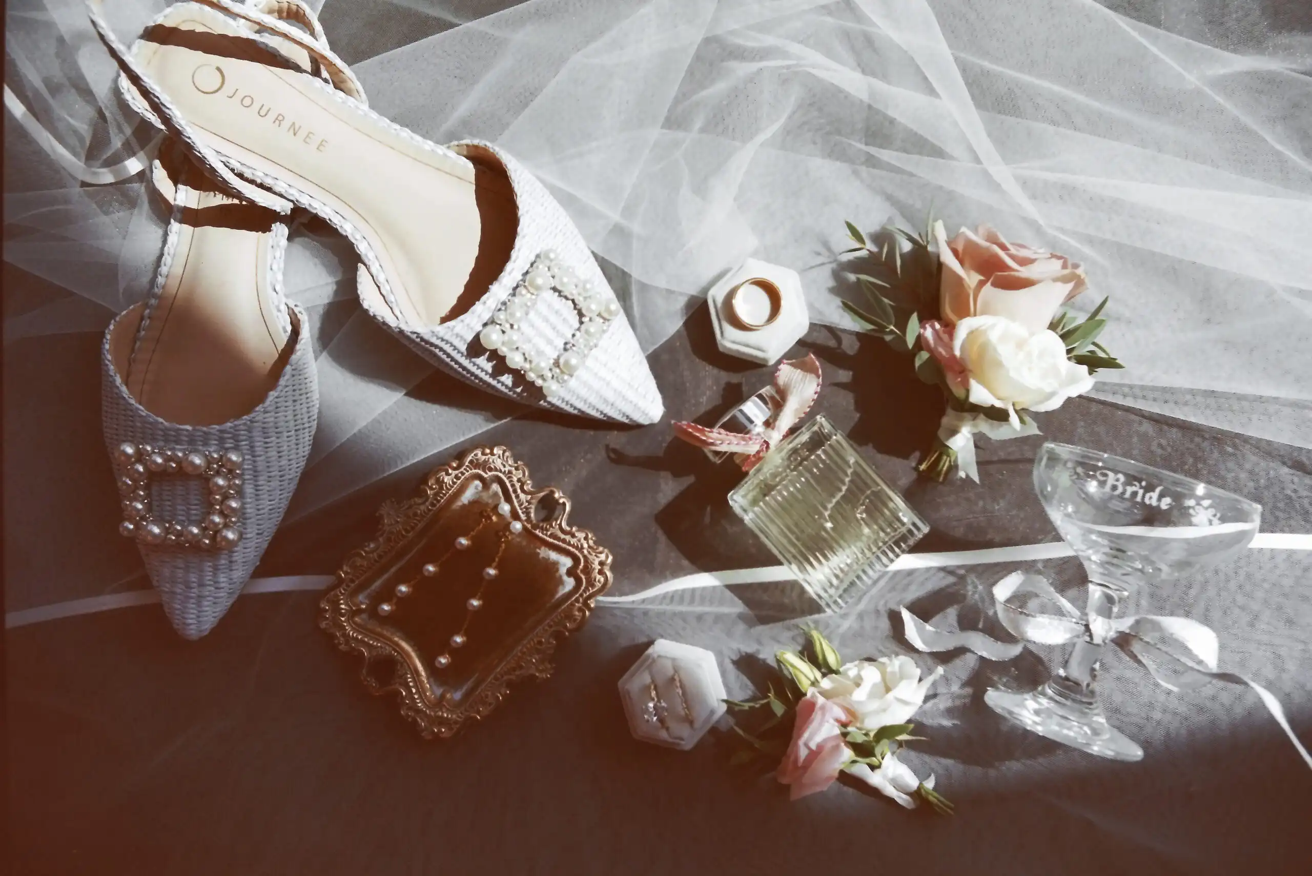 Bridal shoes, rings, perfume and boutonnieres laid out on the veil before a wedding, shot on 35mm film