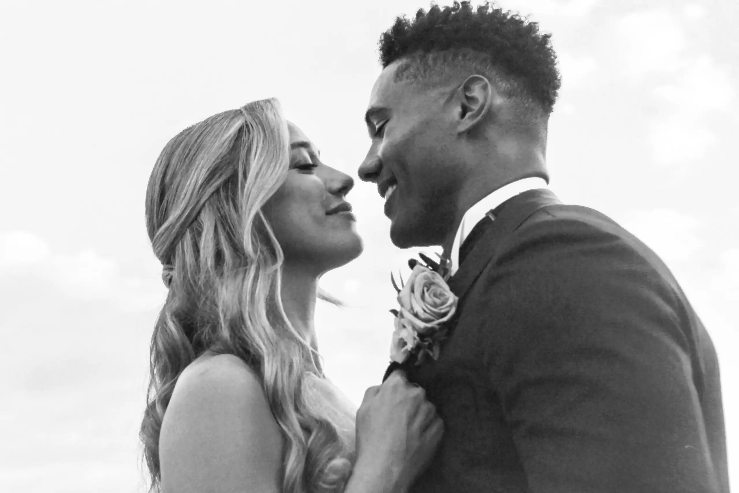 Bride straightening the groom's boutonniere before a kiss at their wedding, in black and white on 35mm film