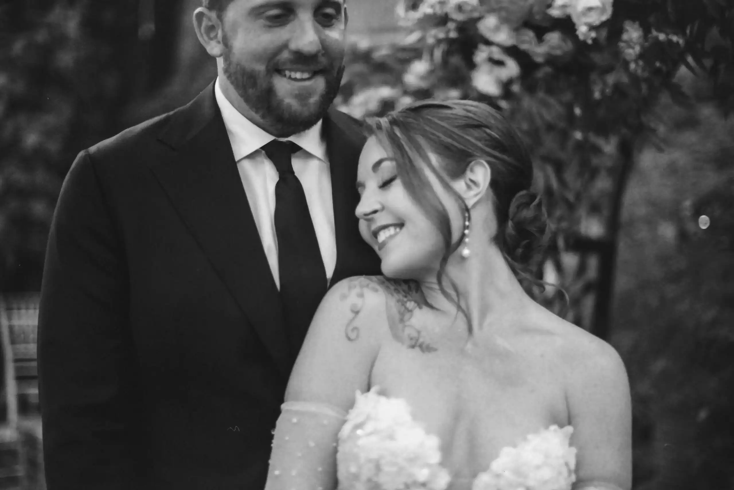 Bride and groom smiling together under a floral arch at their wedding, in black and white on 35mm film at Wahoo! Grill in Decatur, GA