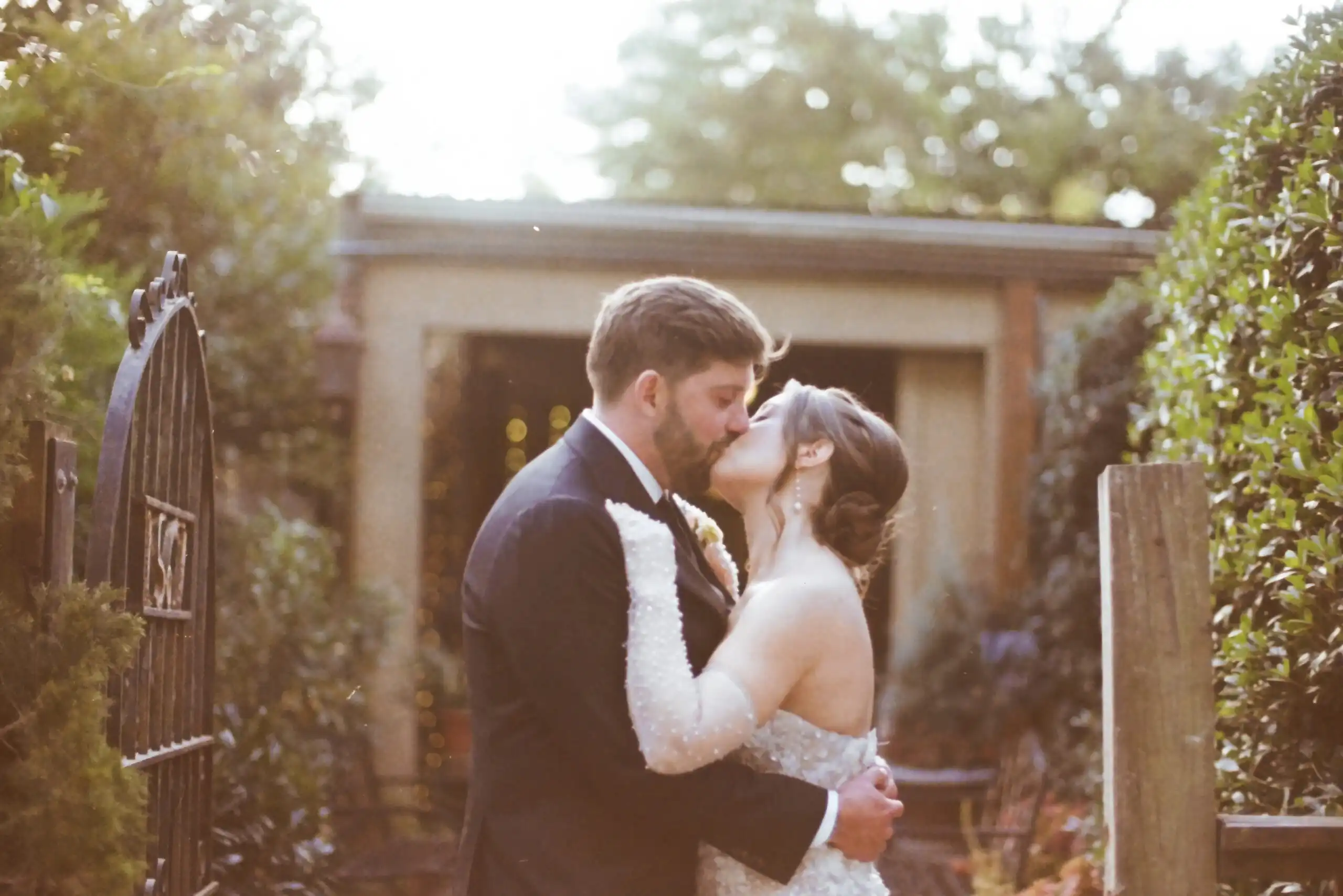 Bride and groom kissing by the garden gate at their wedding, shot on 35mm film