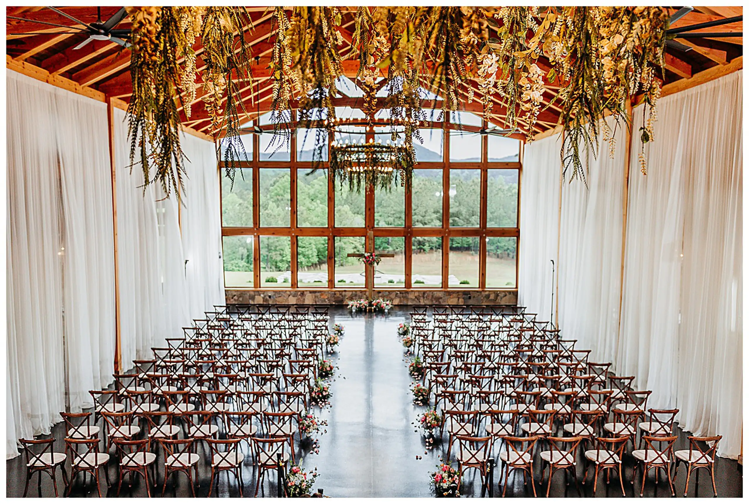 Wedding Ceremony: the aisle set with chairs, greenery hung from the timber ceiling, at a wedding at The Venue at Sharp Mountain in Jasper, GA