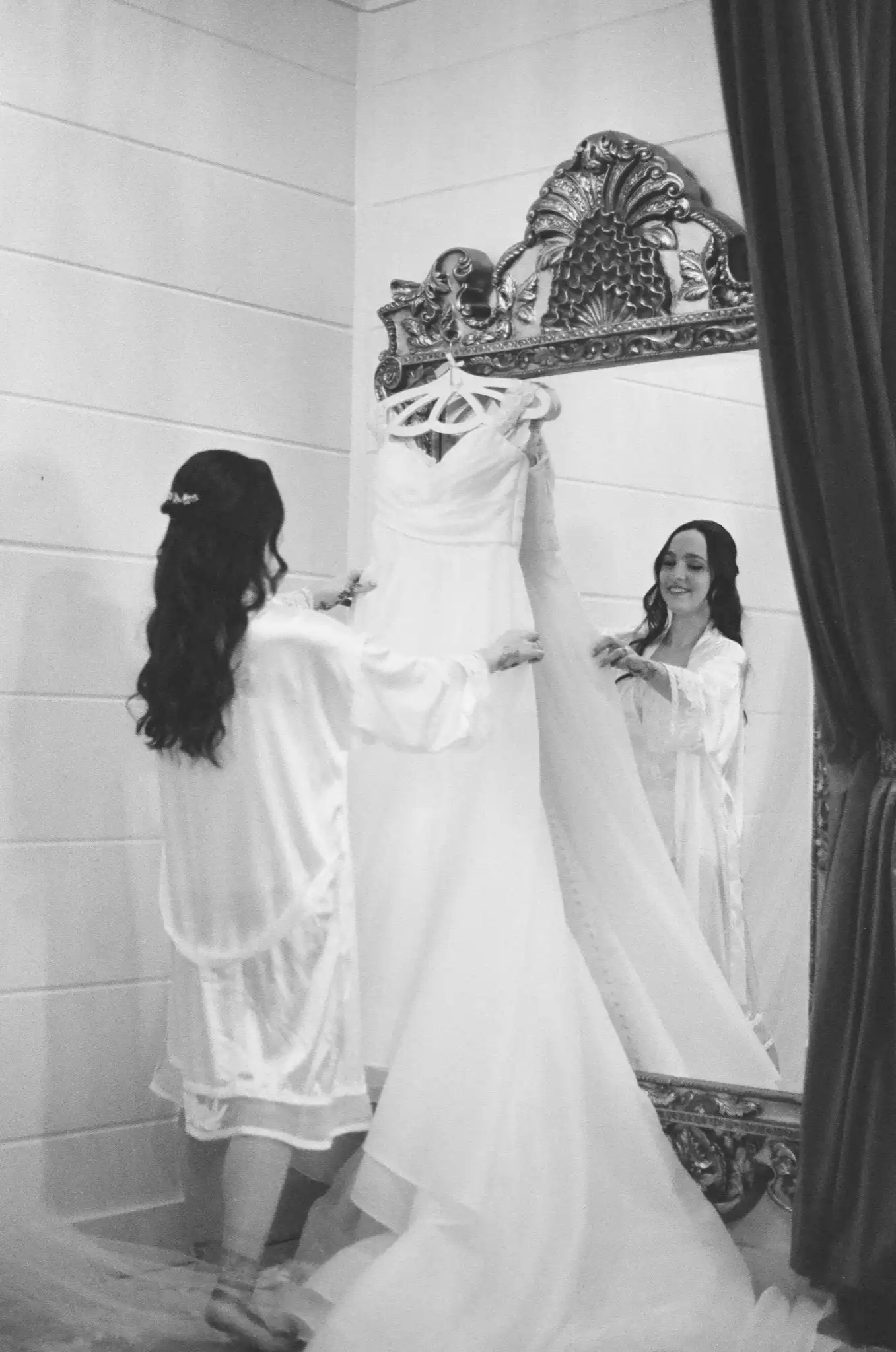 Bride holding up her gown before an ornate mirror in the bridal suite, in black and white on 35mm film at The Venue at Sharp Mountain in Jasper, Georgia