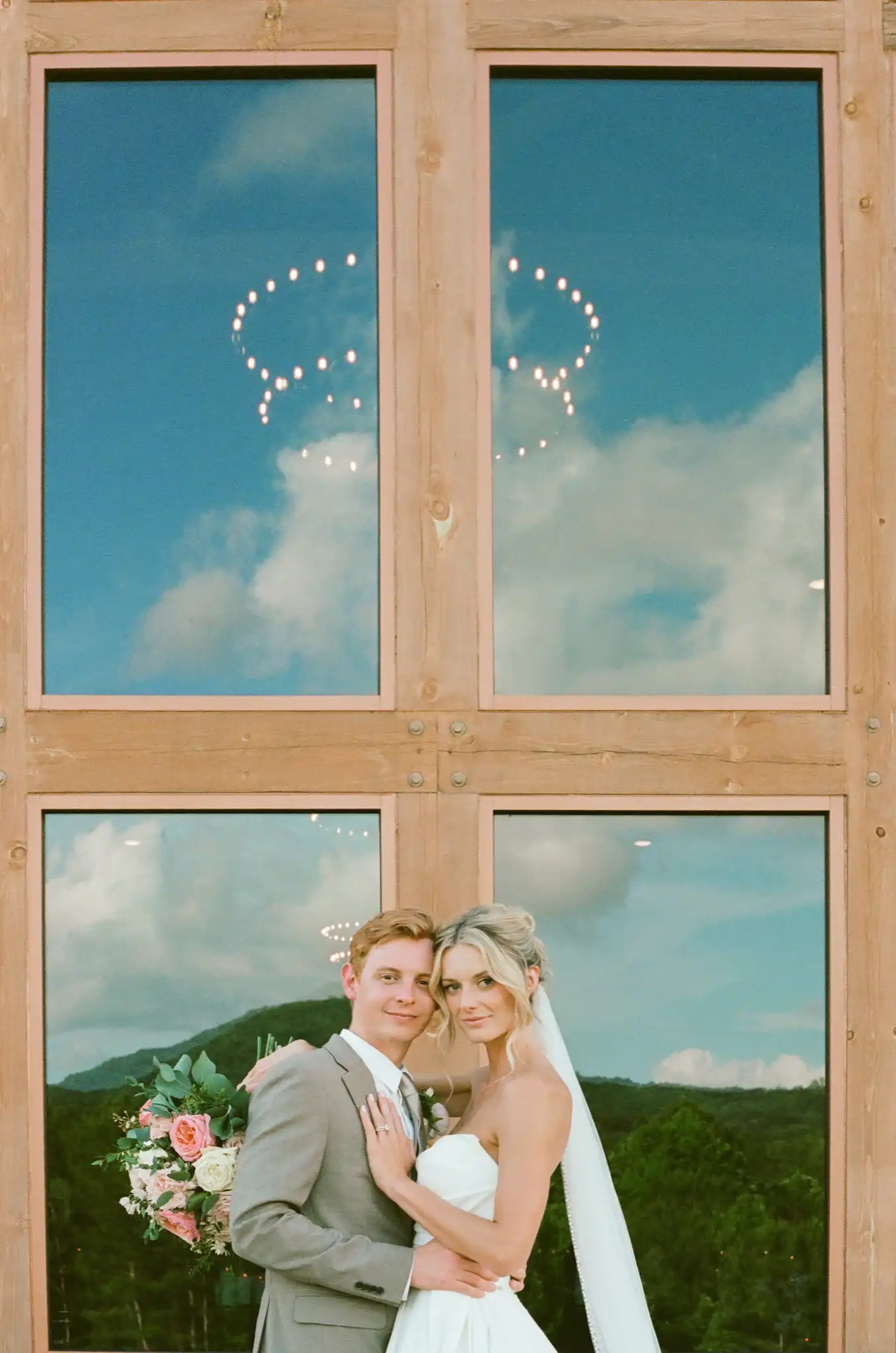 Bride and groom in front of the barn windows with the mountains reflected behind them, shot on 35mm film at The Venue at Sharp Mountain in Jasper, Georgia