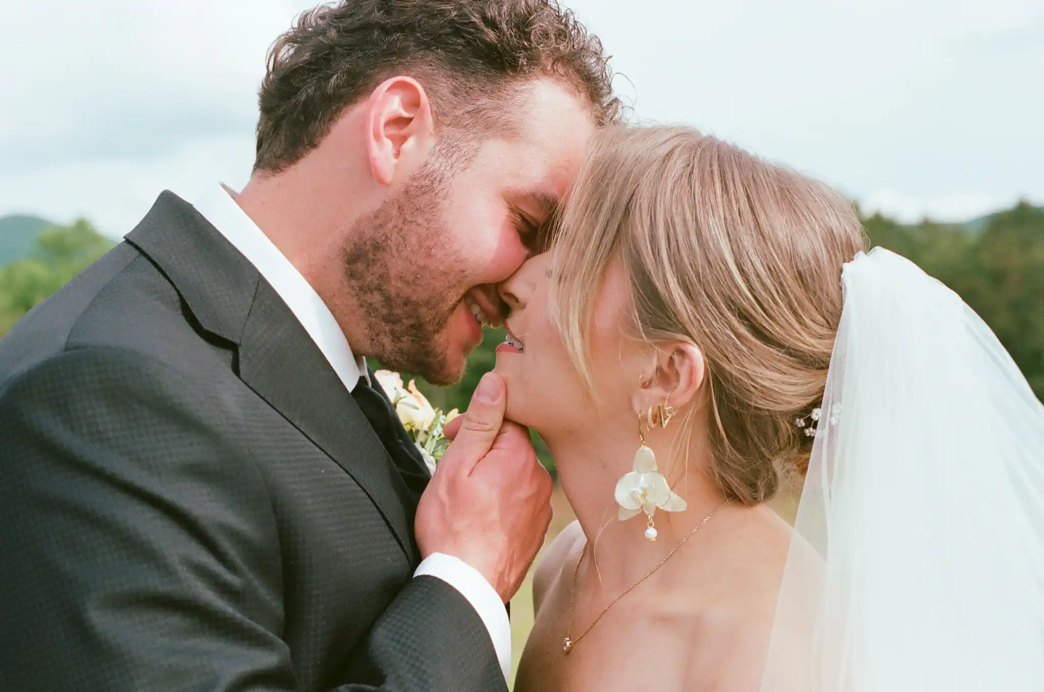 Groom cupping the bride's face as they lean in to kiss, shot on 35mm film at The Venue at Sharp Mountain in Jasper, Georgia