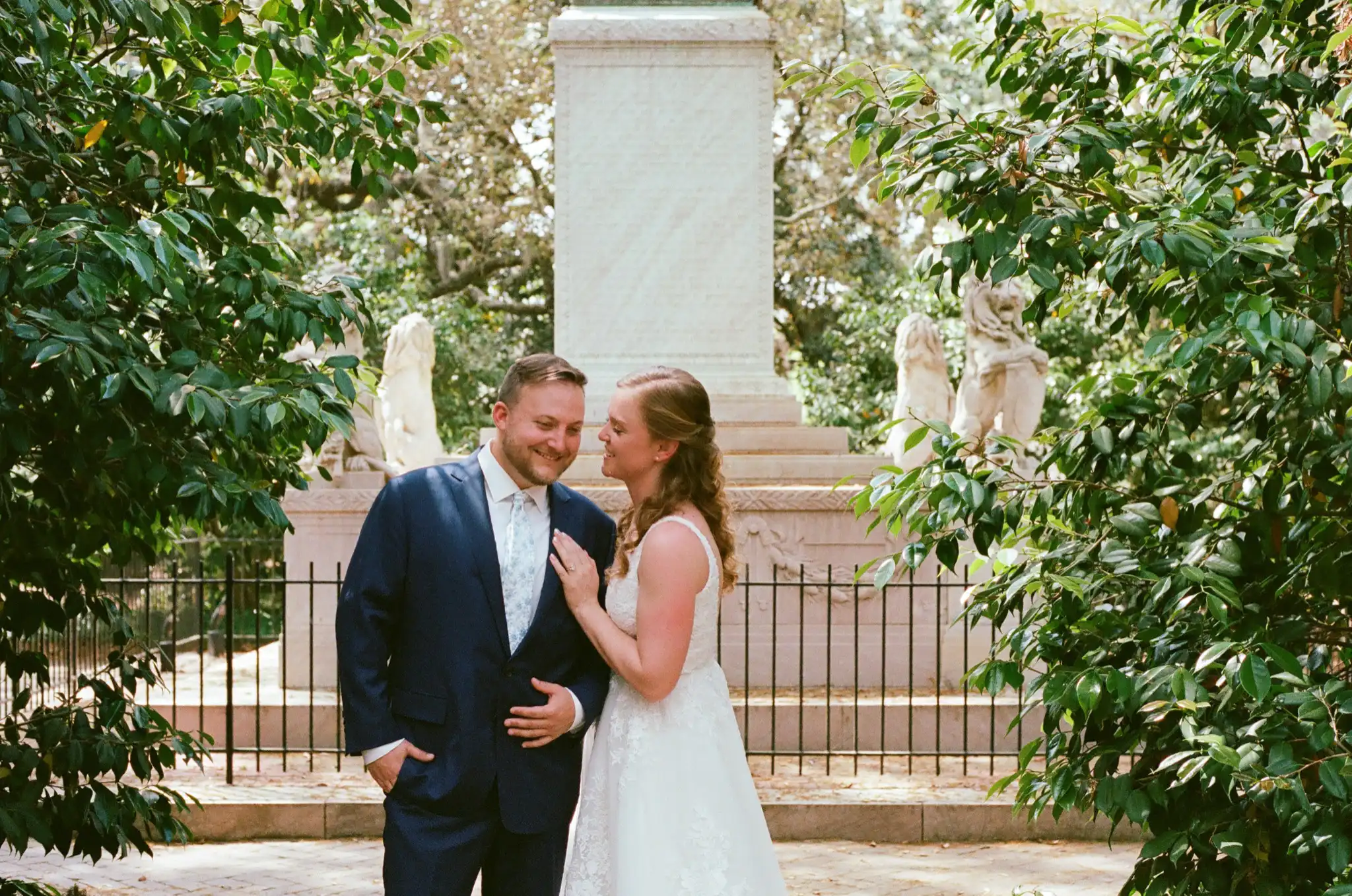 Bride and groom laughing together by the monument in a historic square, shot on 35mm film in Savannah, Georgia