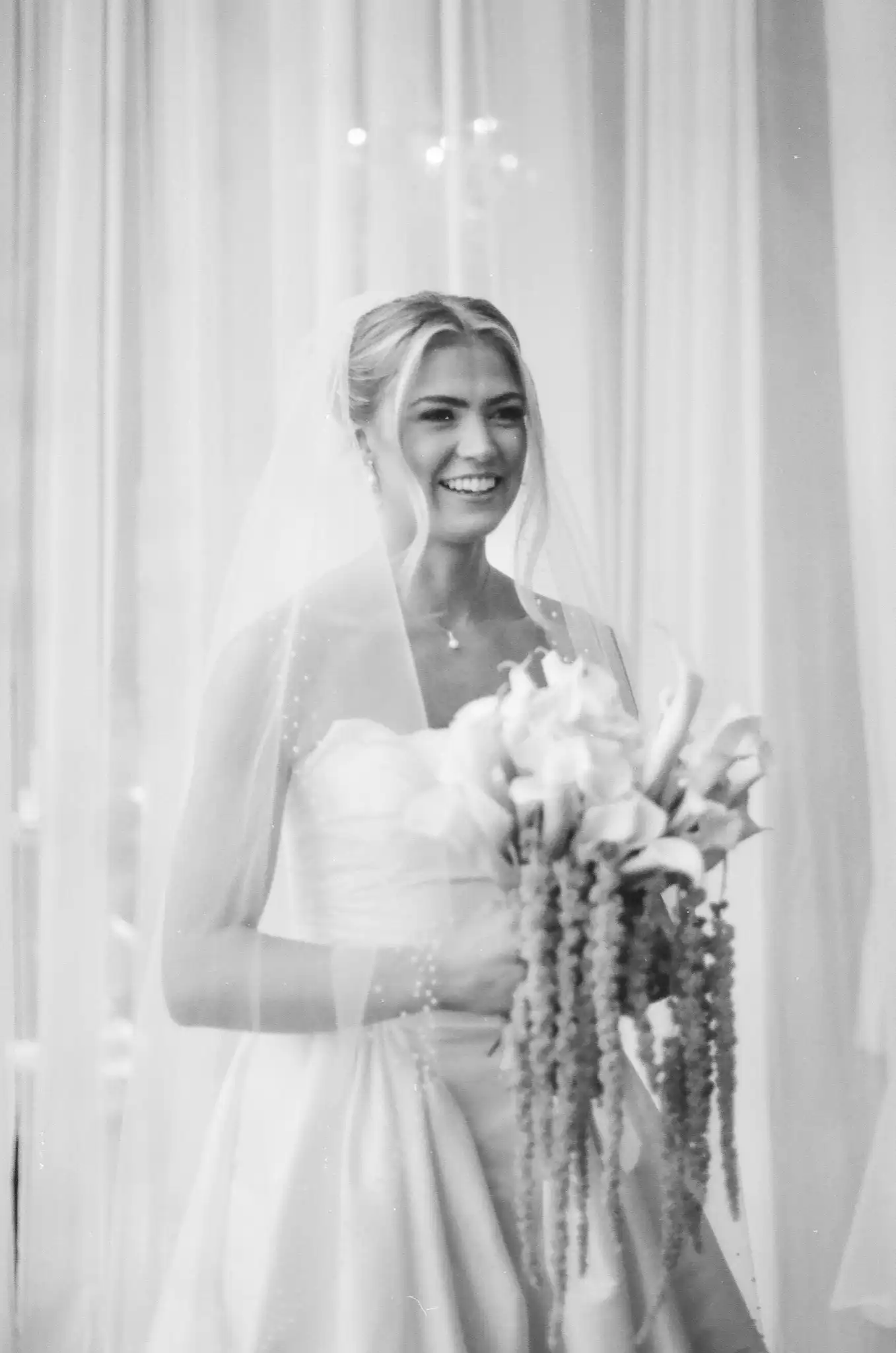 Bride laughing behind her veil with a calla lily and amaranthus bouquet, in black and white on 35mm film at The Venue at Sharp Mountain in Jasper, Georgia