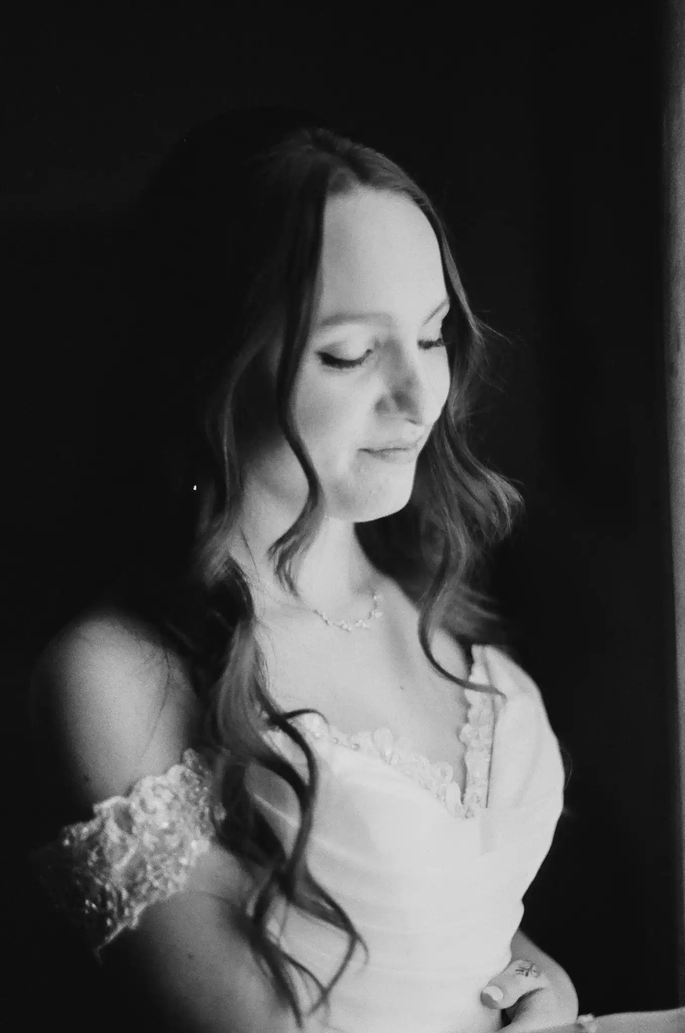 Bride in window light in a lace off-shoulder gown before her wedding, in black and white on 35mm film at The Venue at Sharp Mountain in Jasper, Georgia