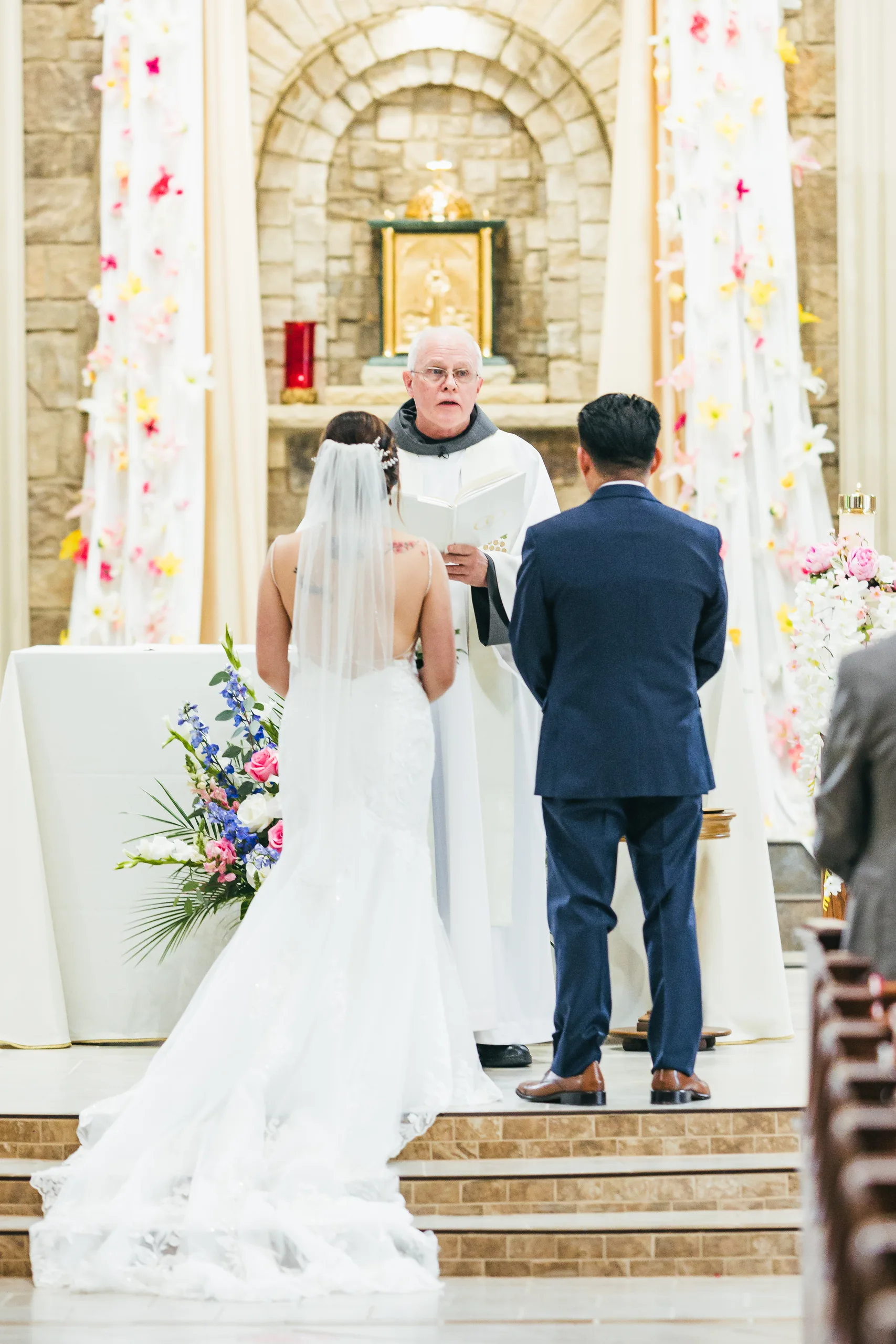 Wedding Ceremony: standing before the priest at the altar at their wedding at Holy Cross Catholic Church in Atlanta, GA