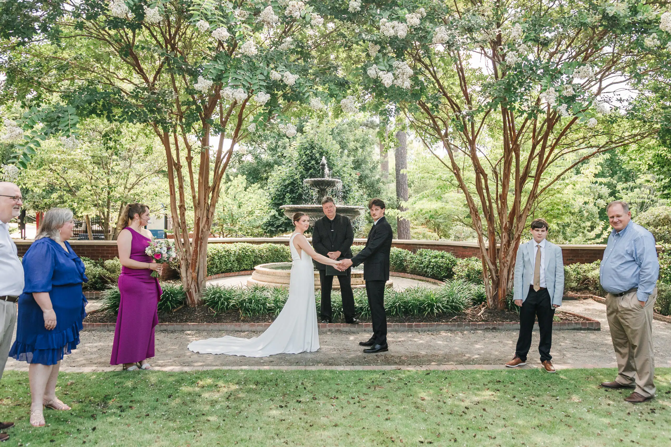 Wedding Ceremony: the vows at the fountain with their guests looking on, at their elopement at Brooke Street Park in Alpharetta, GA