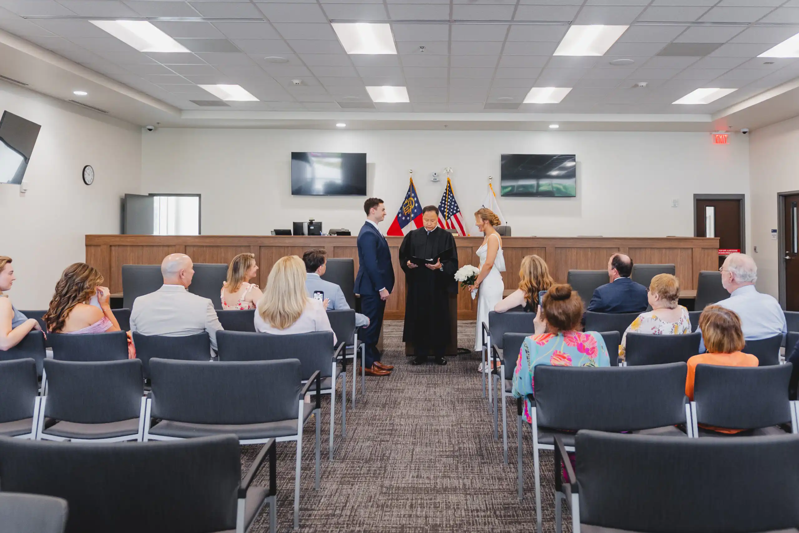 Wedding Ceremony: the vows before the judge, flags behind them, at their courthouse wedding at Brookhaven City Hall in Brookhaven, GA