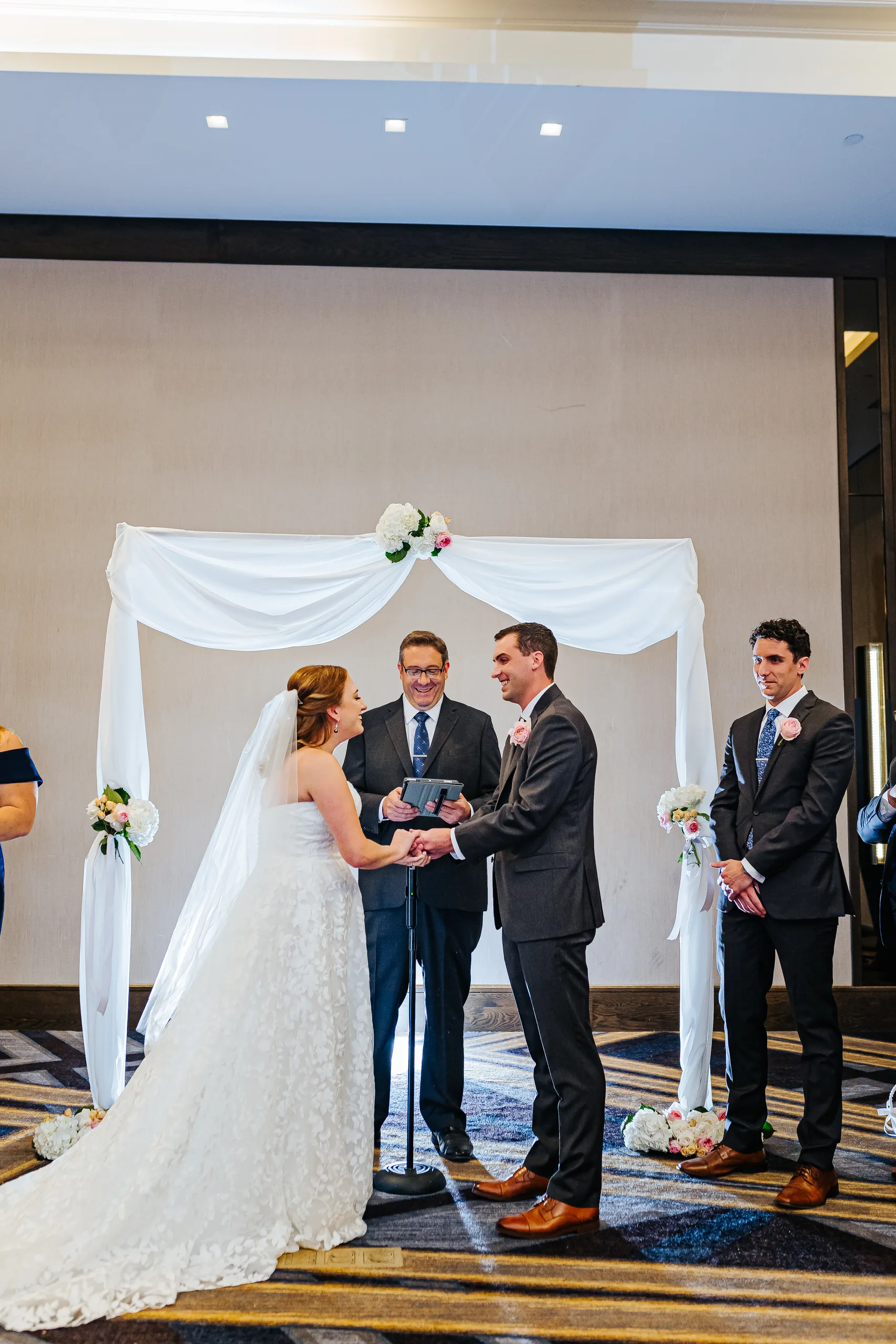Wedding Ceremony: exchanging vows under the white draped arch at their wedding at the Omni Hotel at The Battery in Atlanta, GA