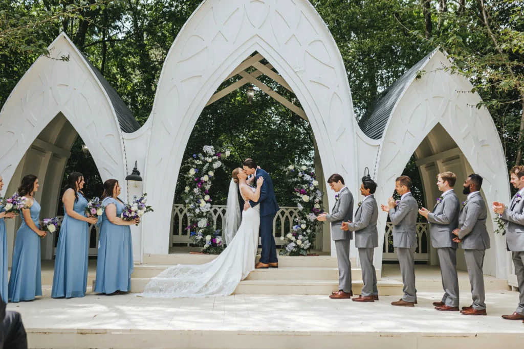 Wedding Ceremony: the first kiss under the chapel's three white arches, at their wedding at The Wildflower 301 in Greensboro, GA