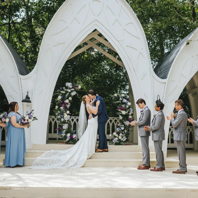 Wedding Ceremony: the first kiss under the chapel's three white arches, at their wedding at The Wildflower 301 in Greensboro, GA