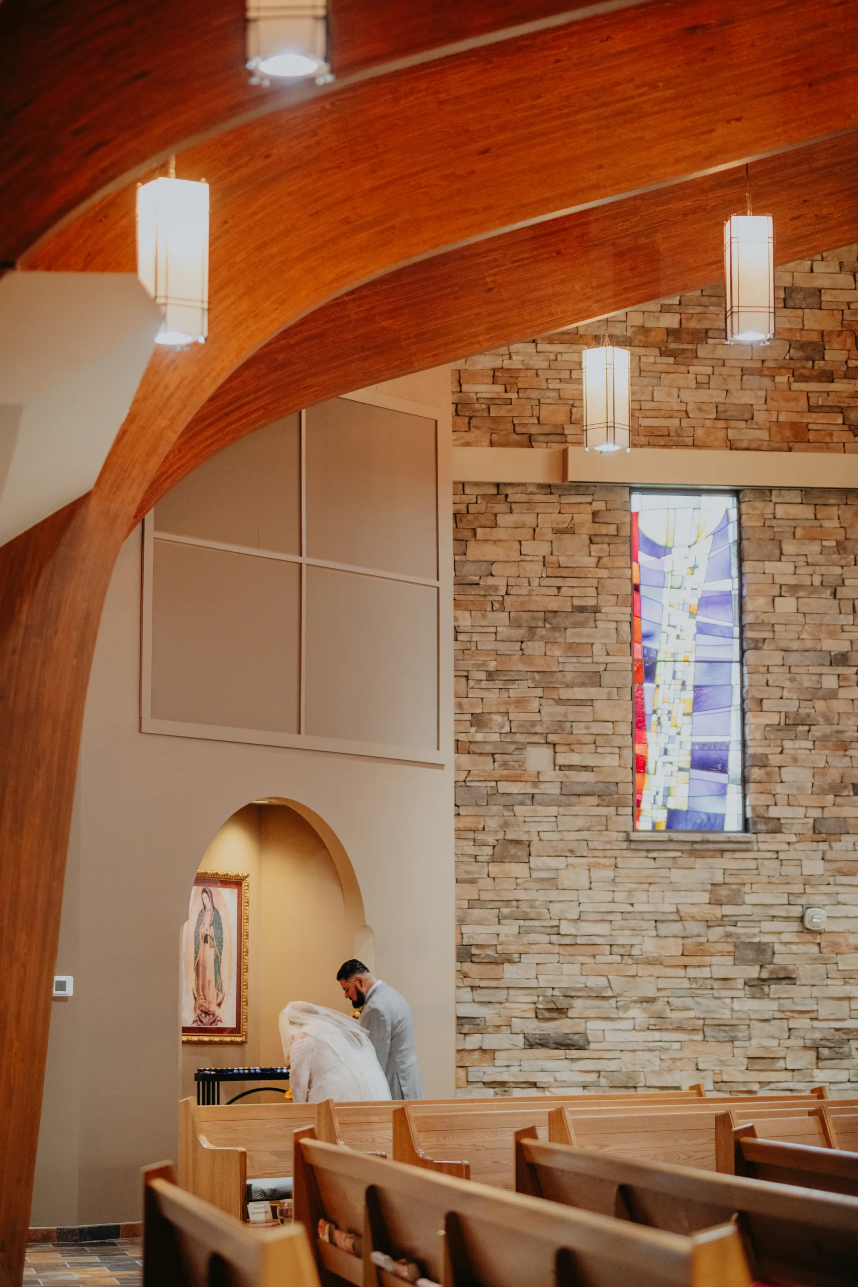 Wedding Ceremony: the couple offering flowers to Mary at the image of Our Lady of Guadalupe, at their wedding at St. Lawrence Catholic Church in Lawrenceville, GA